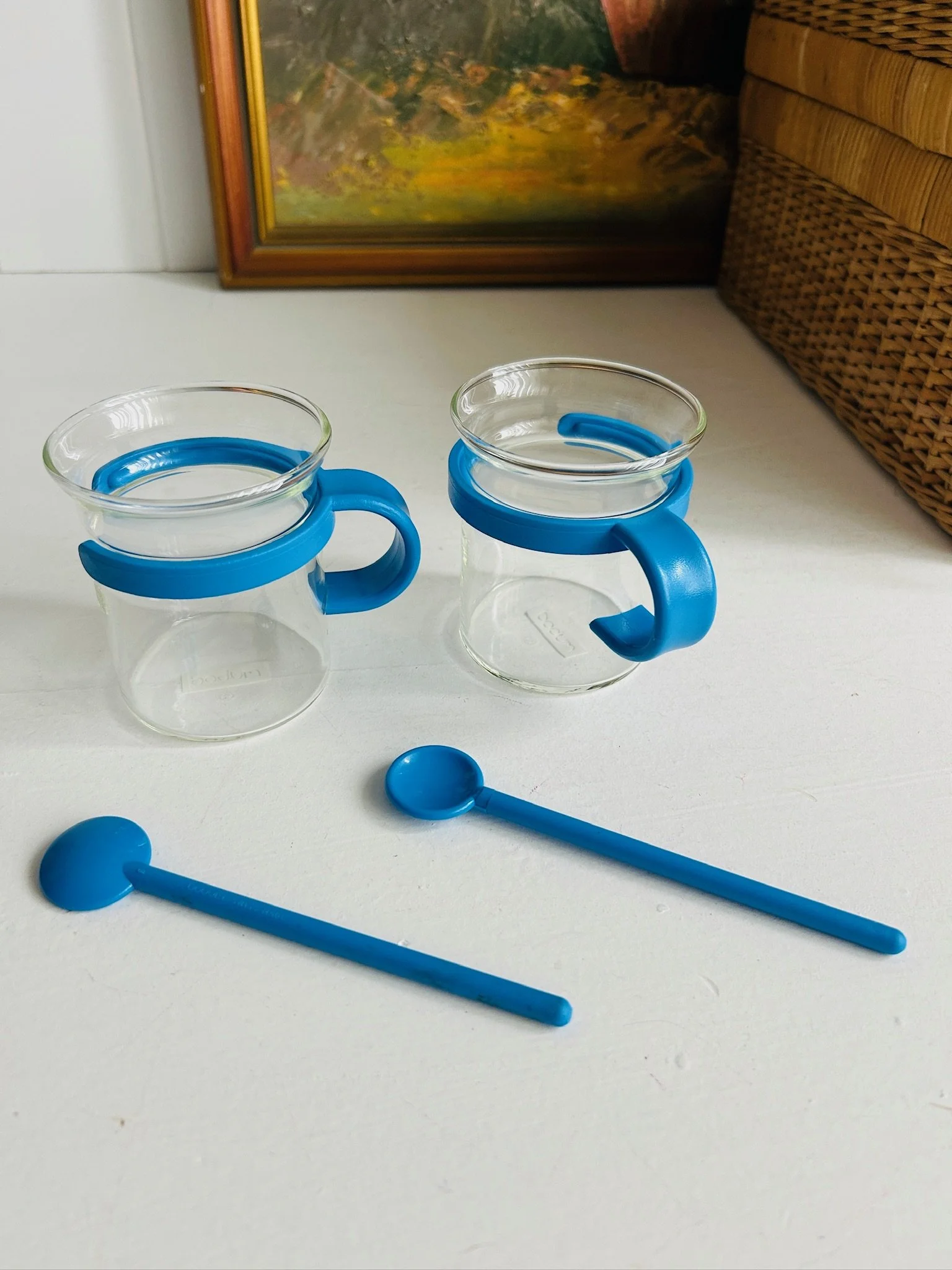 Pair of vintage Bodum Picard cups with blue holders and matching blue spoons displayed side by side.