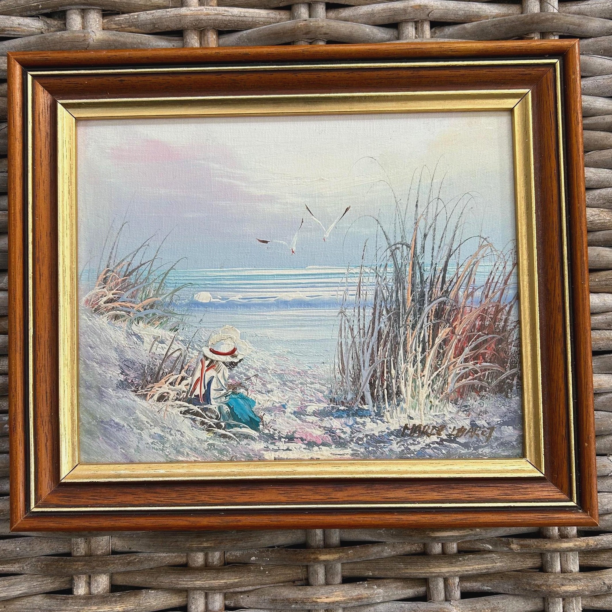 Vintage oil painting of a coastal scene with woman, birds, and waves. Framed and signed. Ideal for beach house decor or vintage-inspired styling.