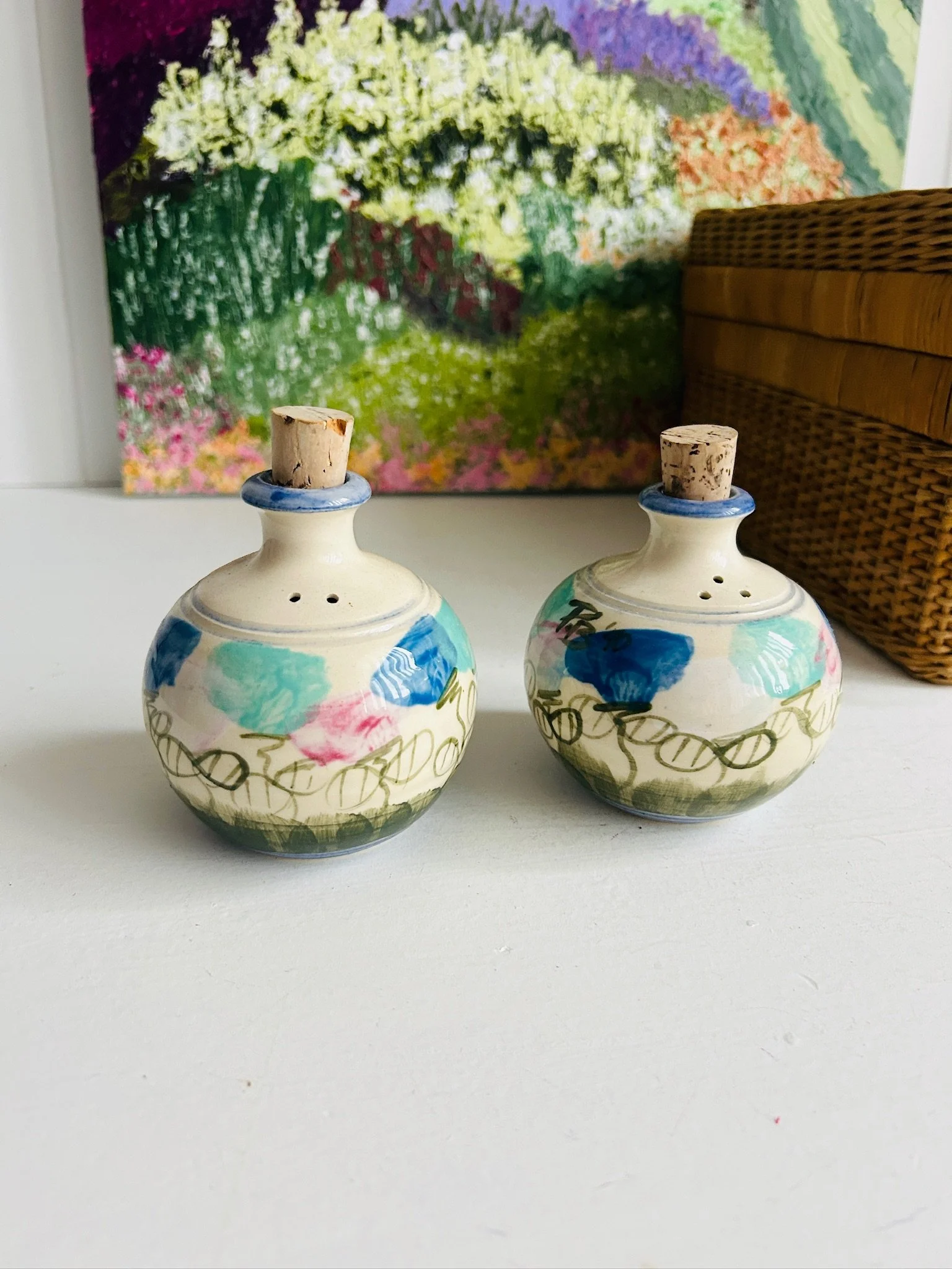 Pair of New Moon Pottery salt and pepper shakers with cork stoppers, hand-painted in blue, aqua, pink, and green on a cream stoneware base