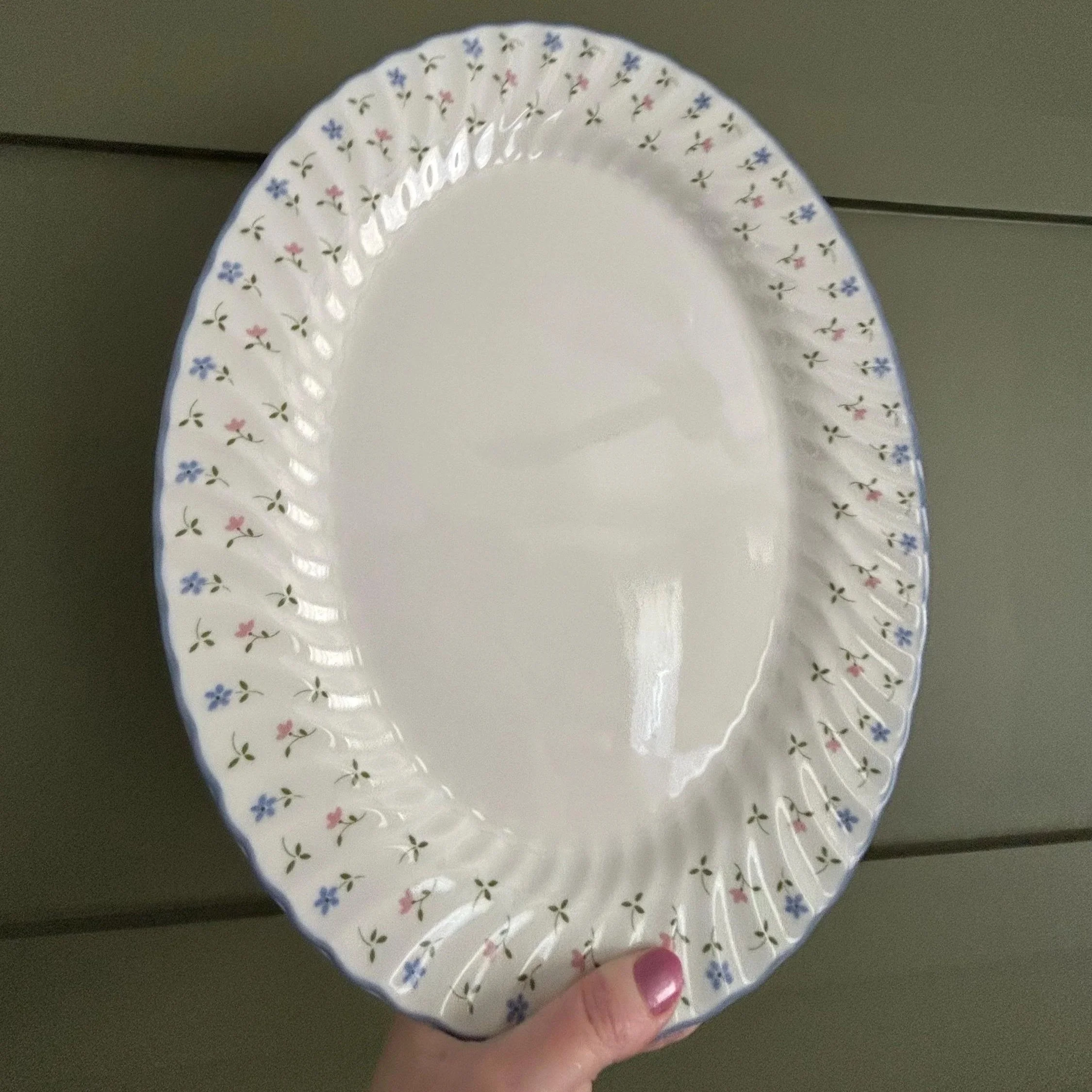Hand holding platter upright, showing full floral border and scalloped edge