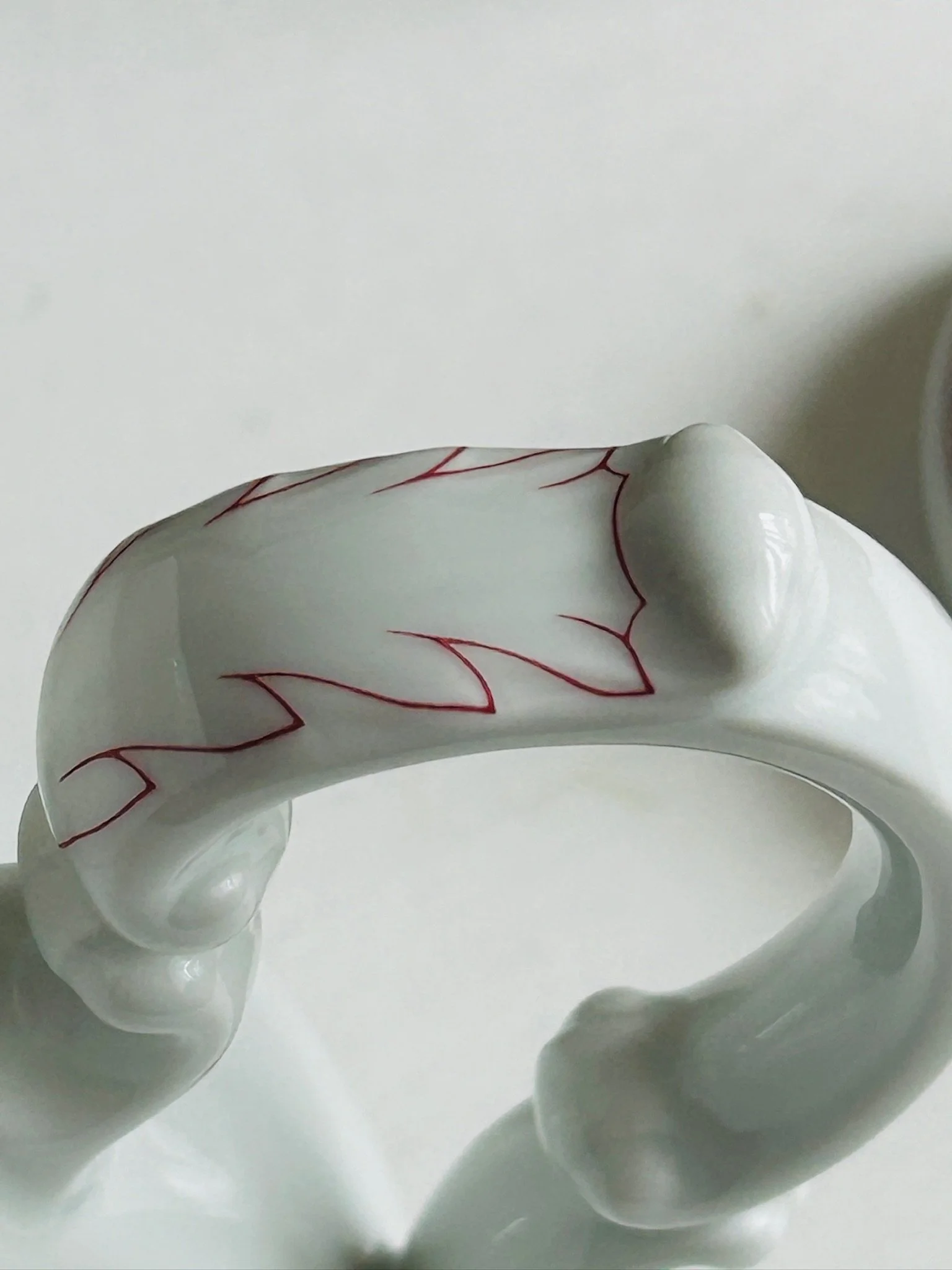 Close-up of the ornate handle with red leaf detail, showing the rococo-inspired shape and glossy white porcelain finish.