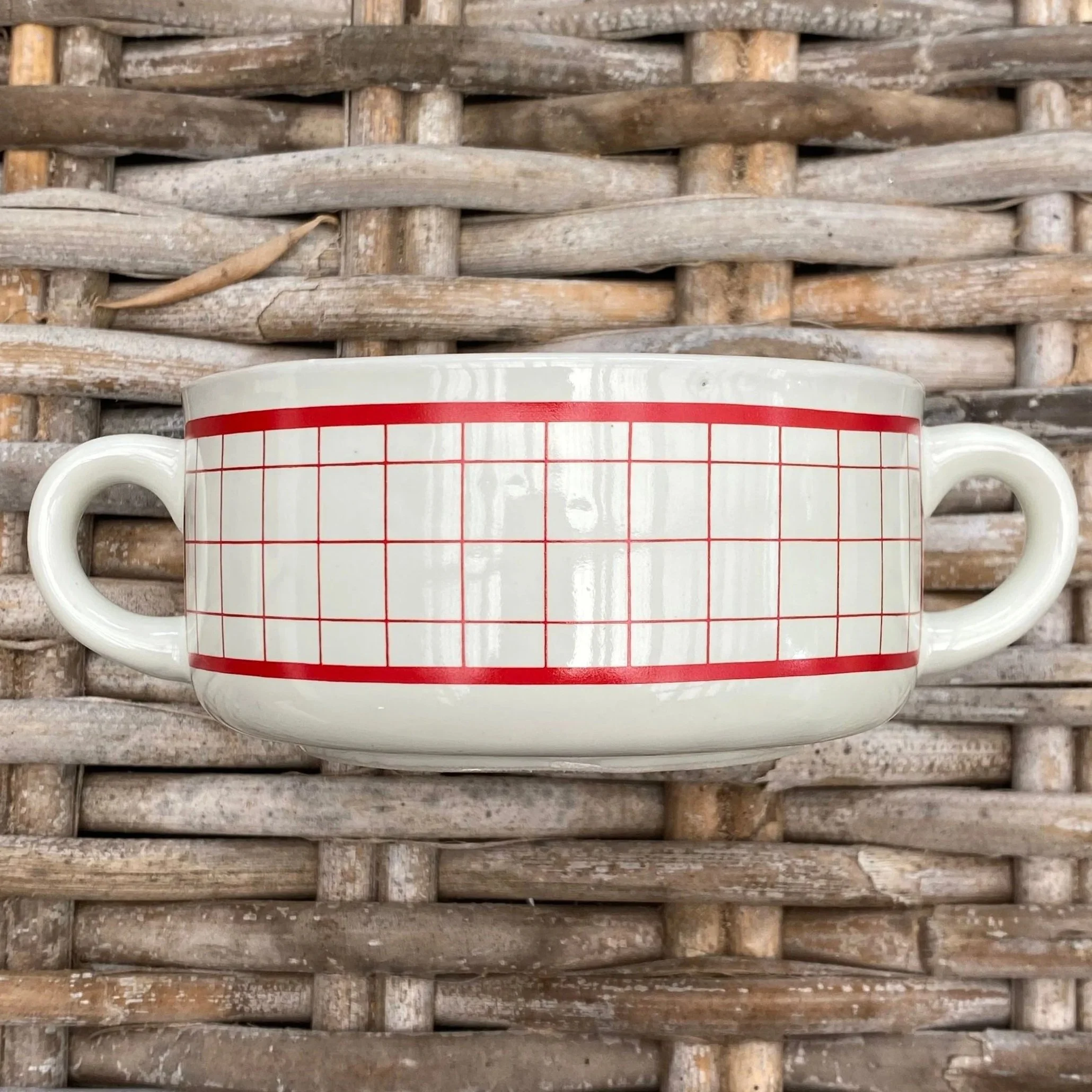 Red grid pattern soup mug with twin handles on woven surface