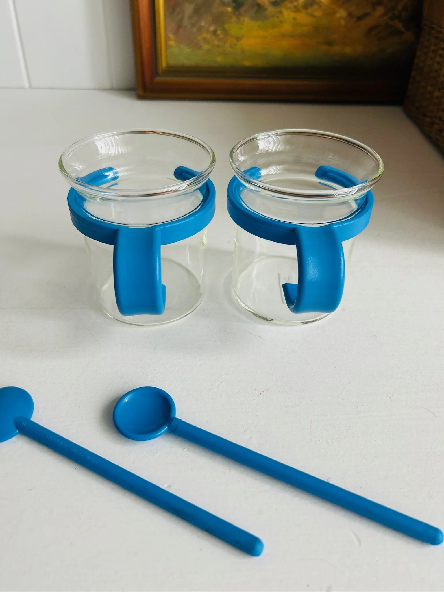 Front view of two Bodum Picard cups with blue holders and matching blue spoons placed in front.