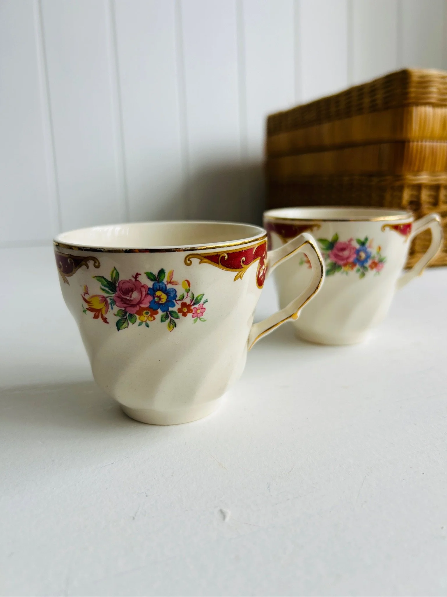 Two vintage English floral teacups displayed side by side on a white surface, showing bouquet pattern and gold trim