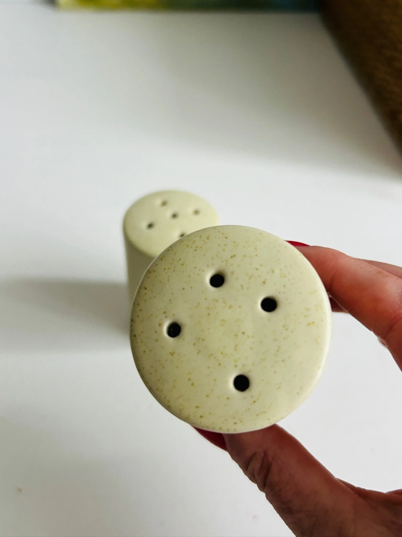 Close-up of one shaker held in hand, showing the four-hole top and cream glaze with fine brown speckles