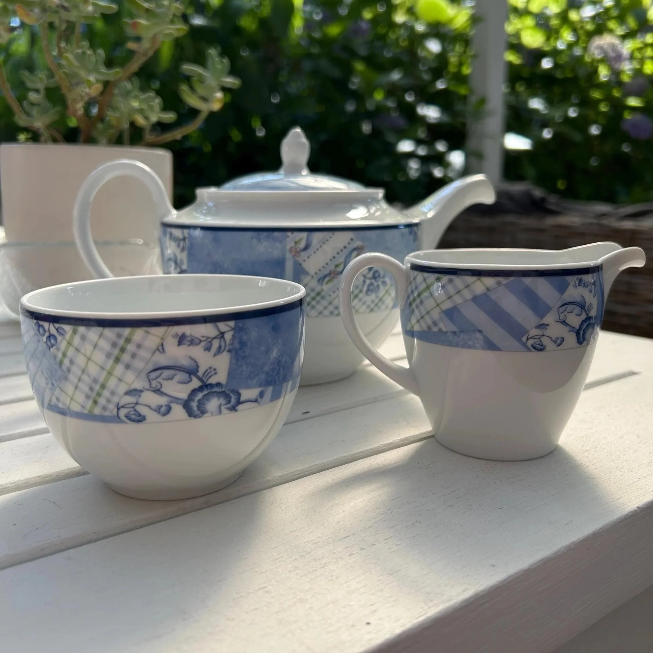 Wedgwood Home Indigo teapot, sugar bowl and creamer arranged together outdoors on a white table