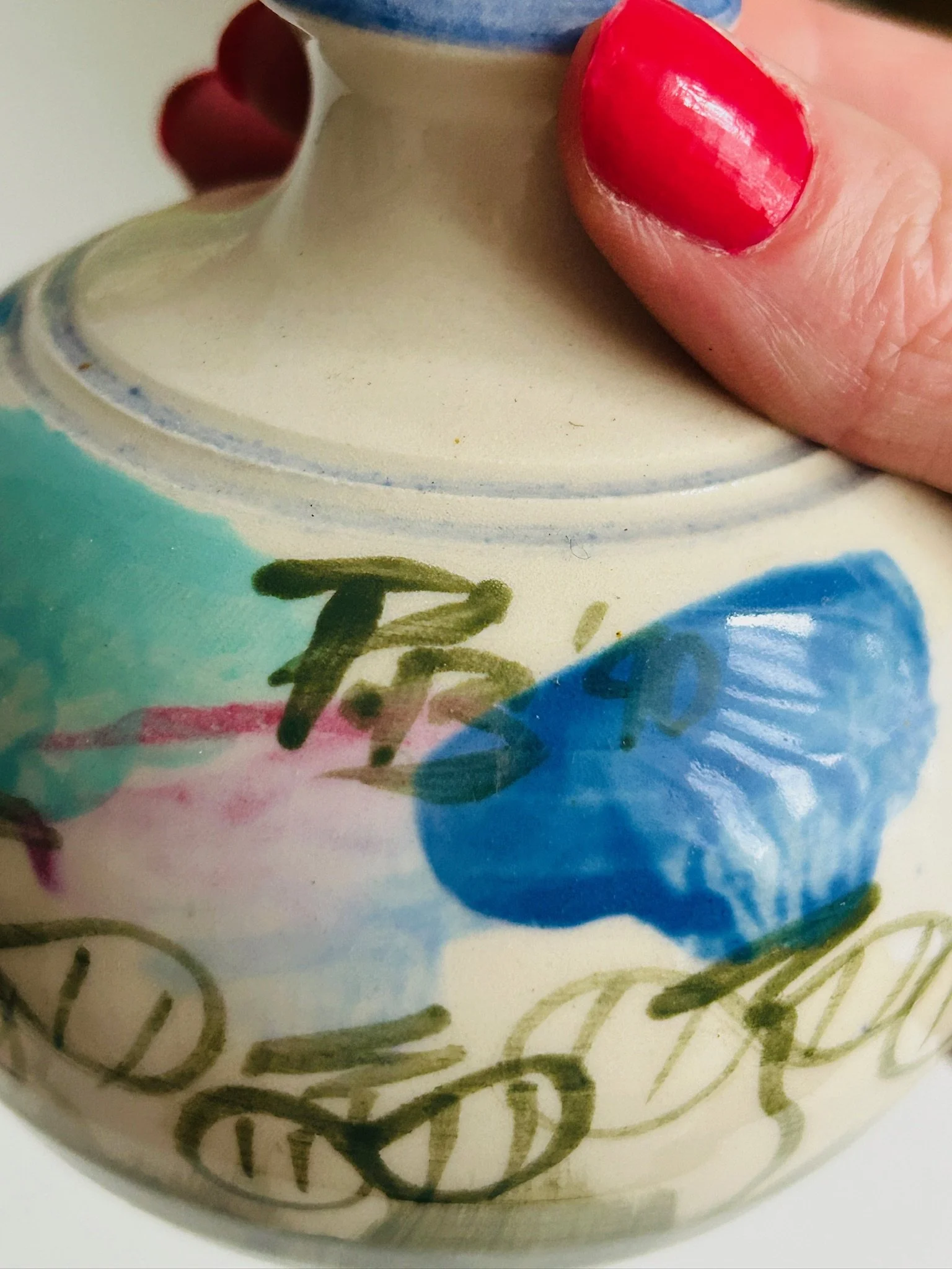 Close-up of hand-painted design with blue floral brushstroke and artist initials on cream glaze