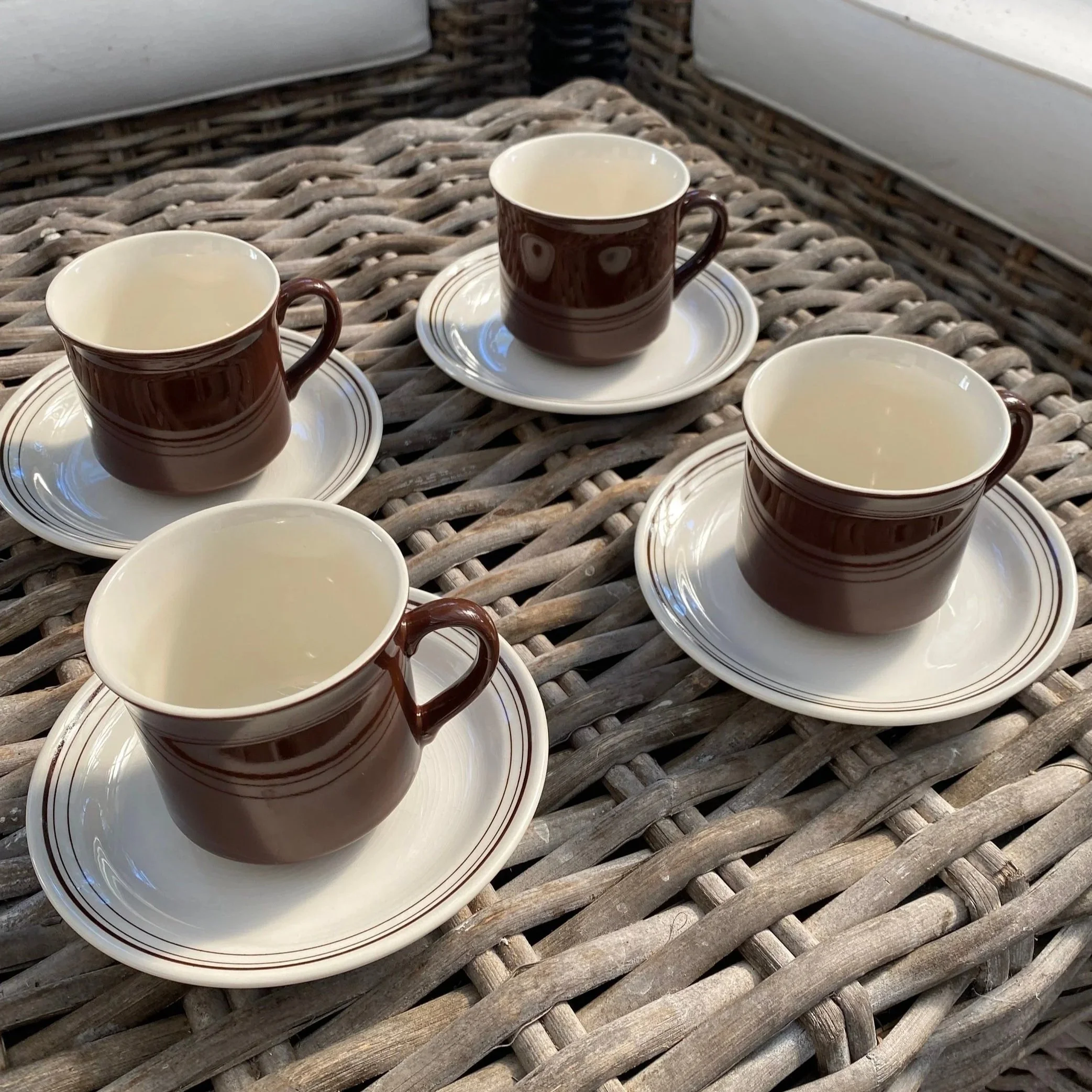 Four Crown Lynn brown cups with cream saucers on wicker table