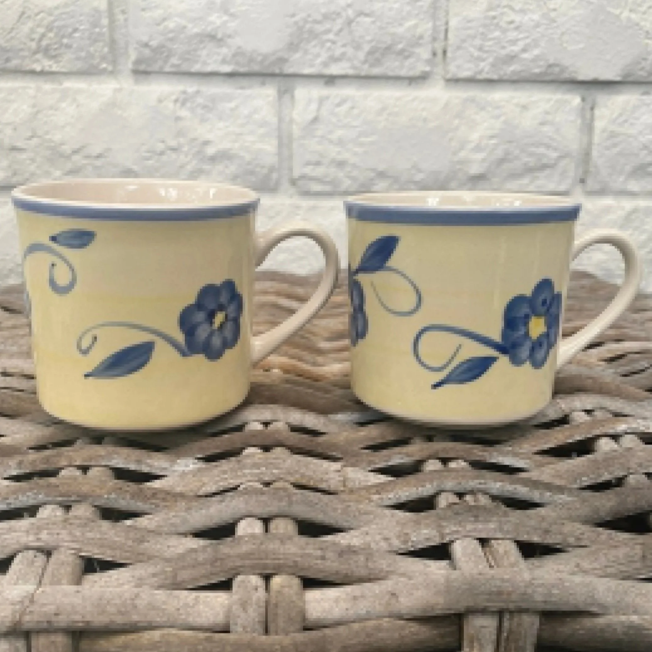 Set of two vintage stoneware coffee mugs with handpainted blue floral design on a soft yellow background