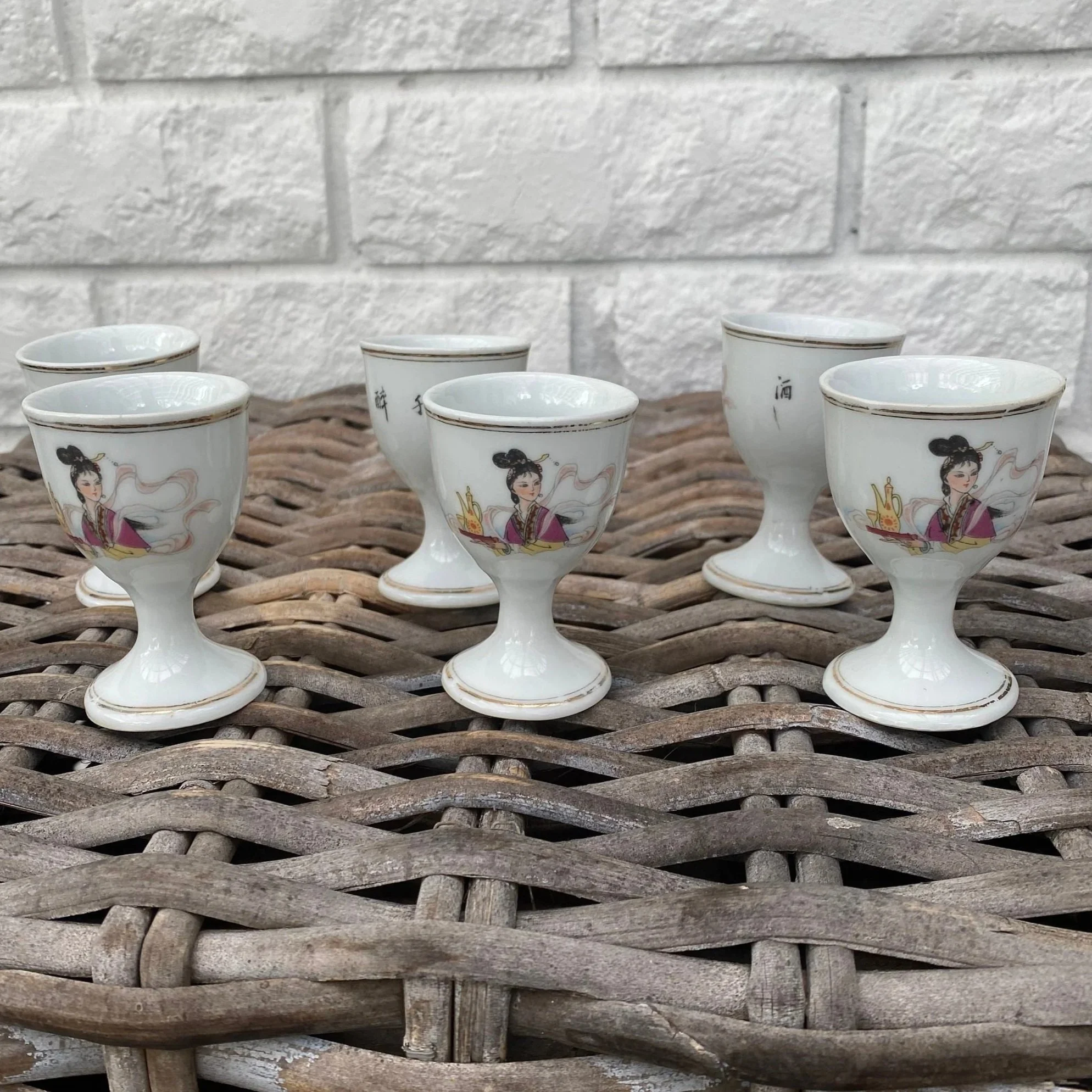 Full view of all six vintage stemmed shot glasses in a group on wicker surface