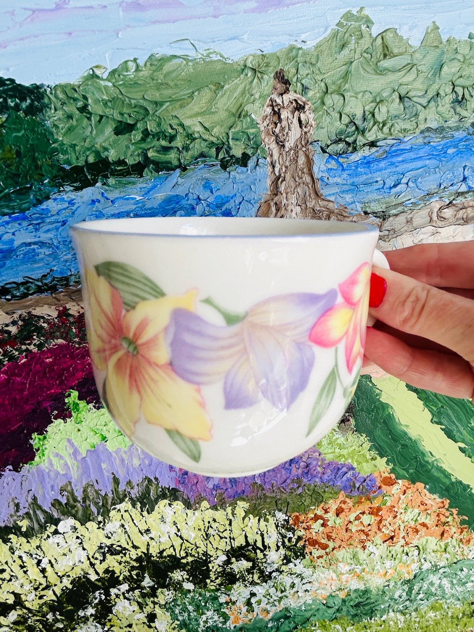 Teacup held in hand against a colourful backdrop, showing the scale, floral decoration, and rounded shape