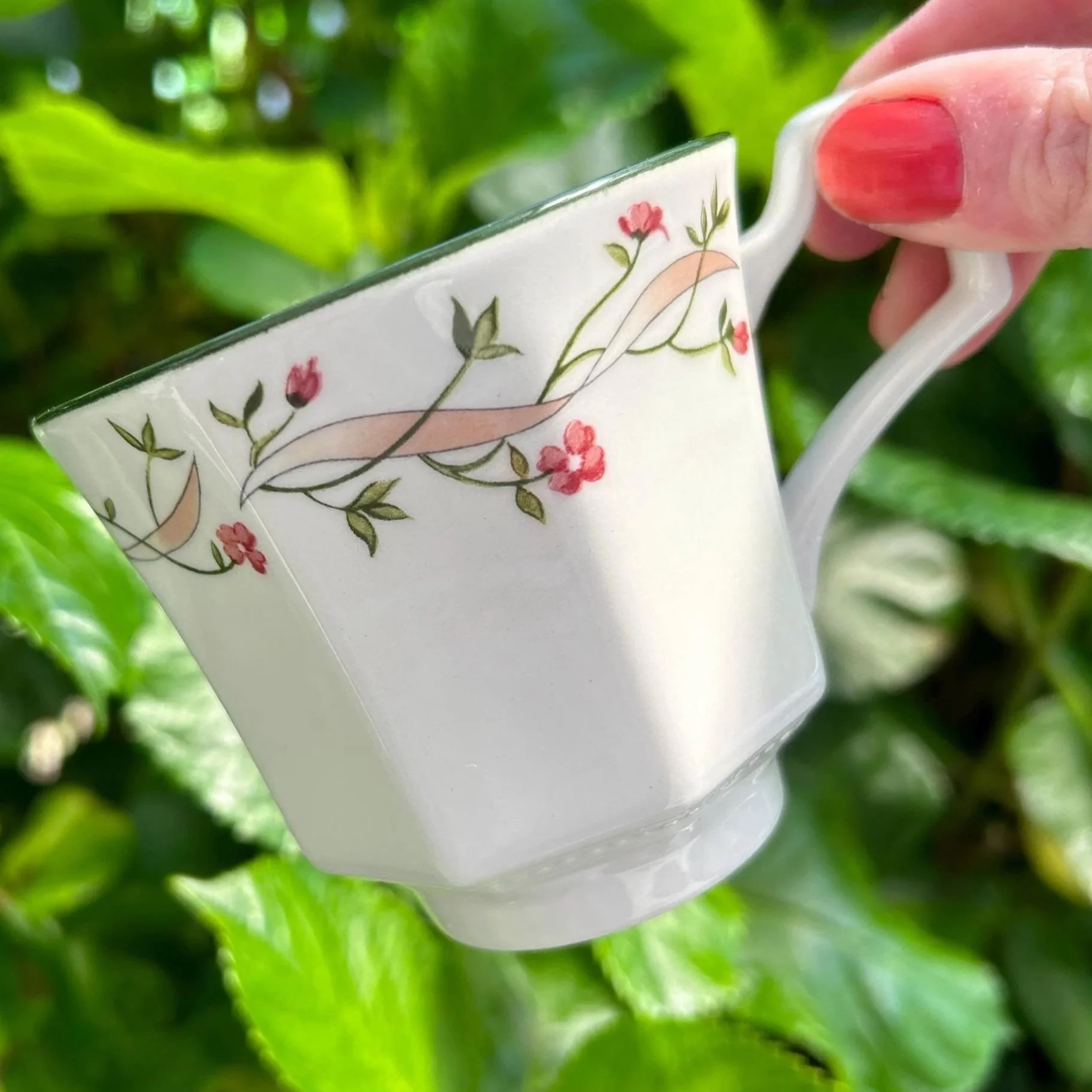 Close-up of tea cup showing pink floral ribbon pattern and soft green rim