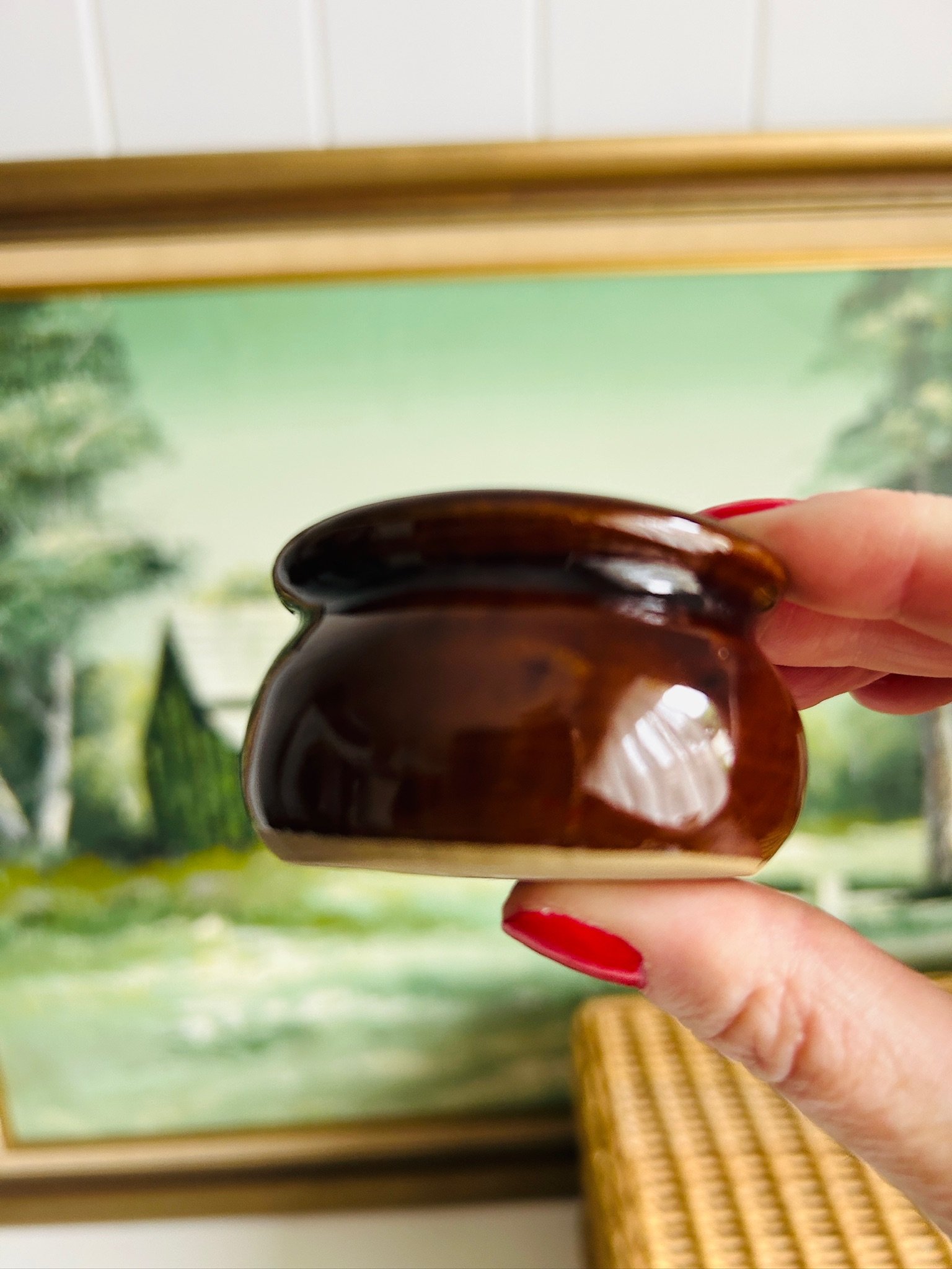 Side view of the glossy brown salt cellar held between fingers against a painted background