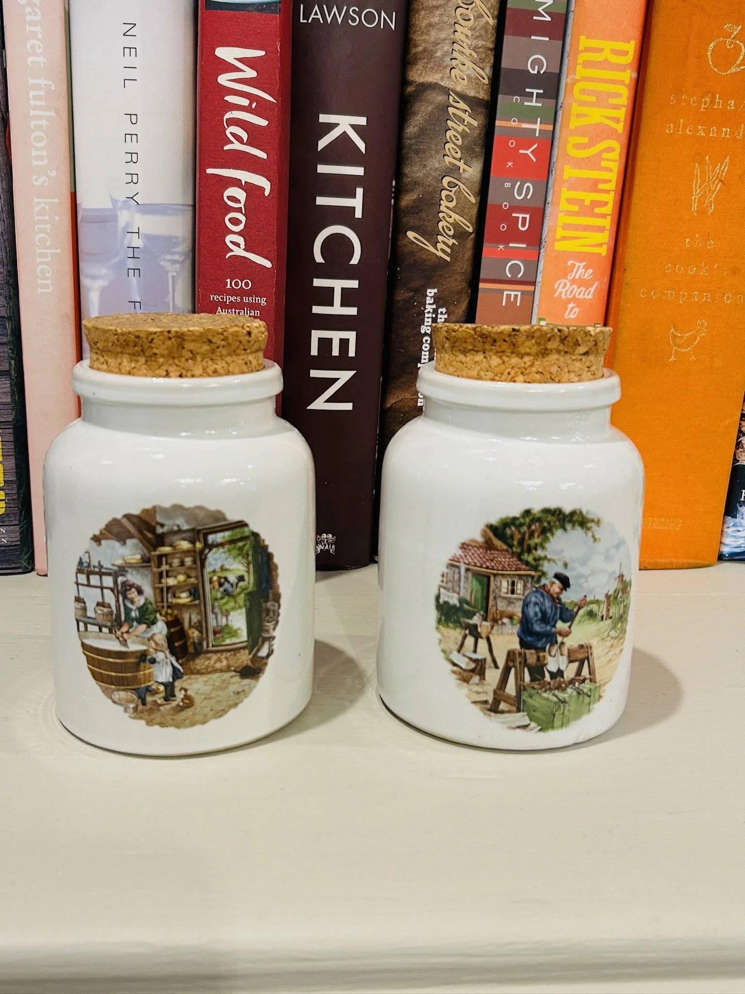 Pair of handcrafted Dutch ceramic mustard pots with cork lids, displayed side by side with hand-painted village scenes on a cream glazed finish.