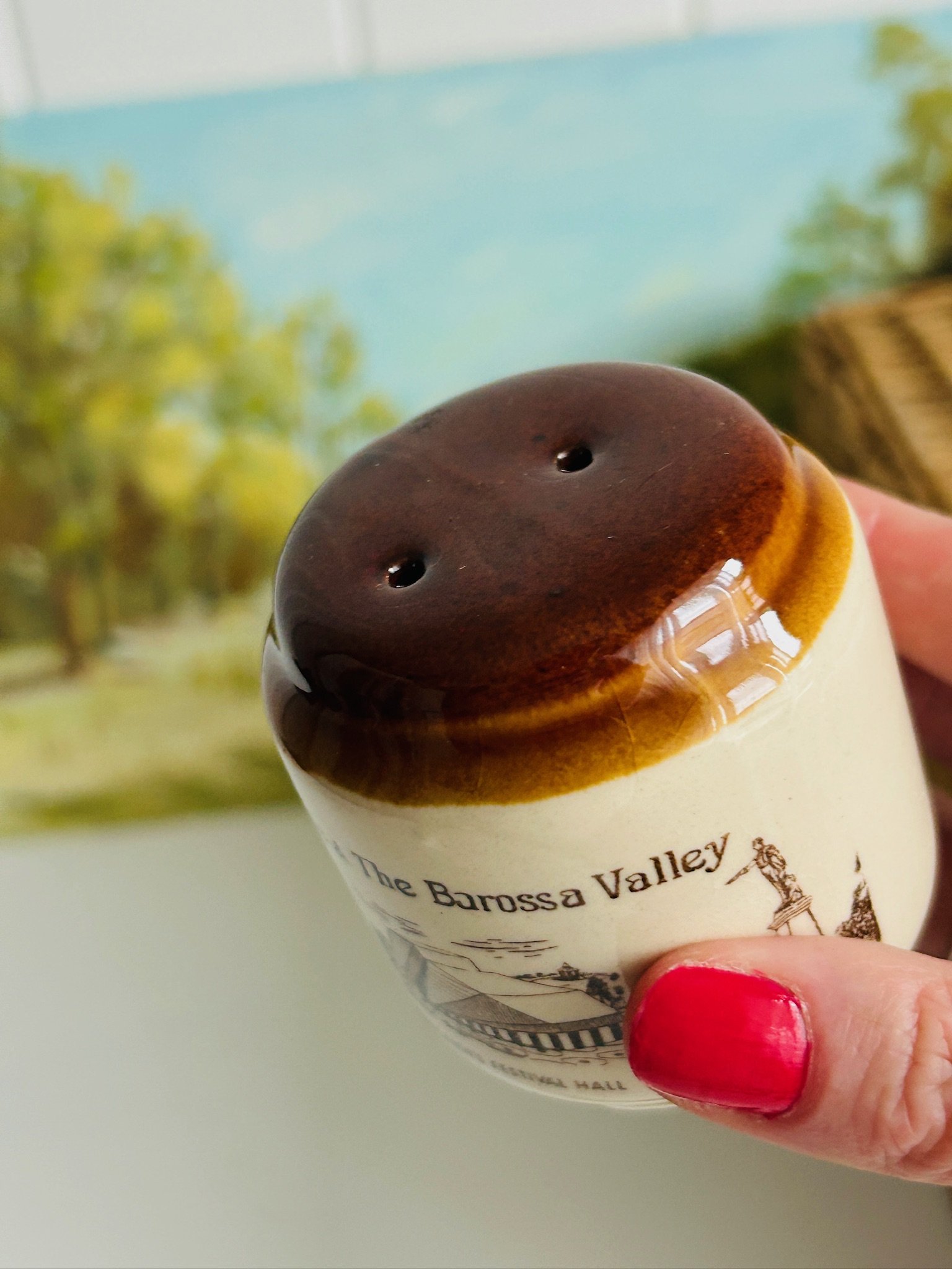 Close-up of one shaker top held in hand, showing the two-hole pattern and rich brown glaze.