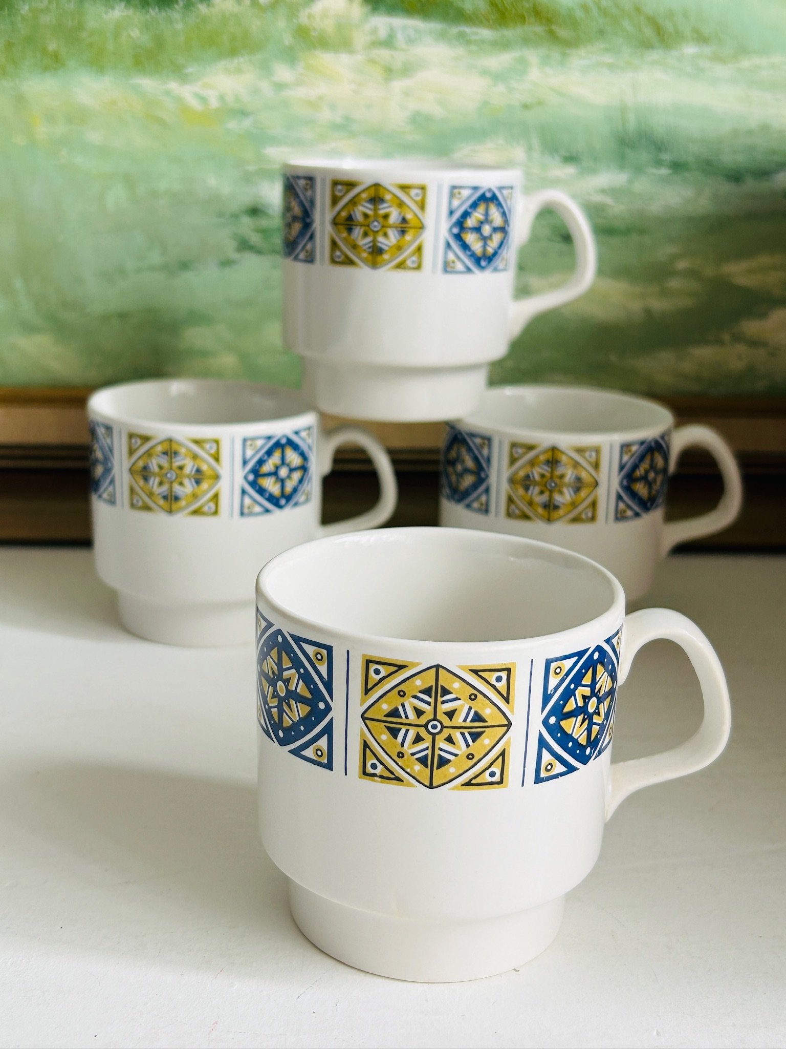 Set of four Staffordshire Midas vintage stackable coffee cups with blue and mustard geometric pattern arranged together on a white surface.