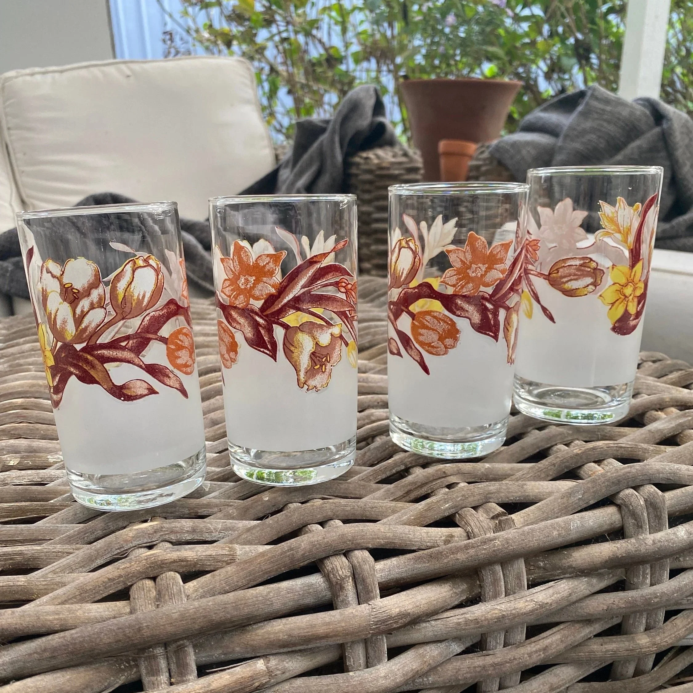 Full set of four frosted floral glasses arranged on wicker surface