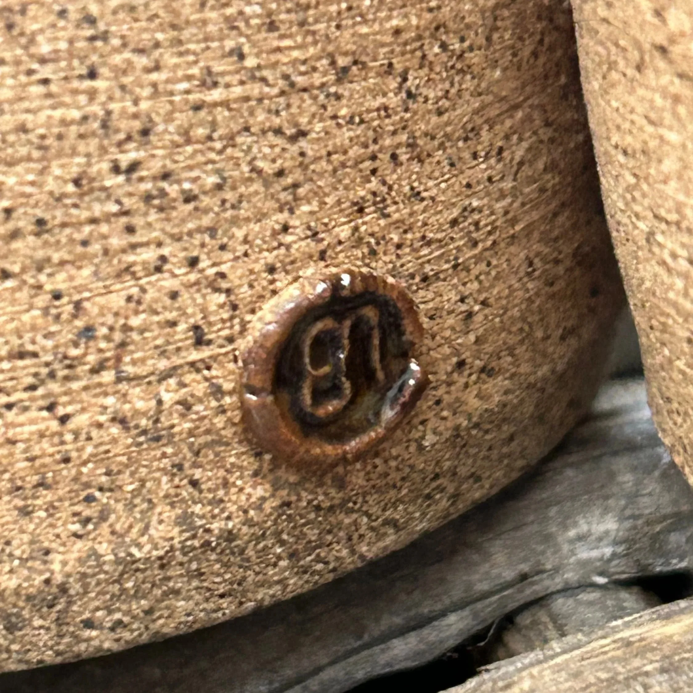 Close-up of artist's "EJ" impressed mark on side of textured stoneware