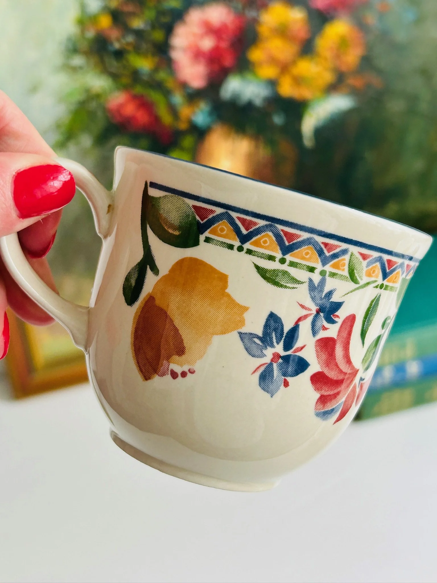 Close-up of the Staffordshire ‘Calypso’ tea cup held in hand, showing the colourful floral design, geometric border, and blue rim detail.