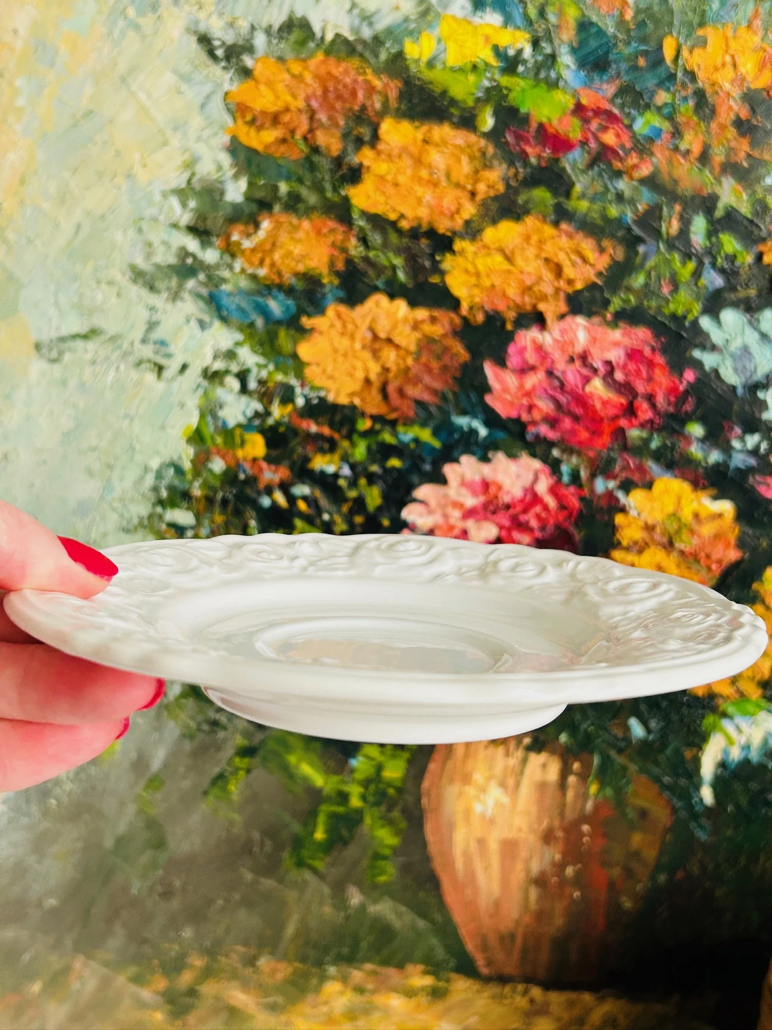 Side profile of the saucer held in hand, showing its shallow form and raised rose border.