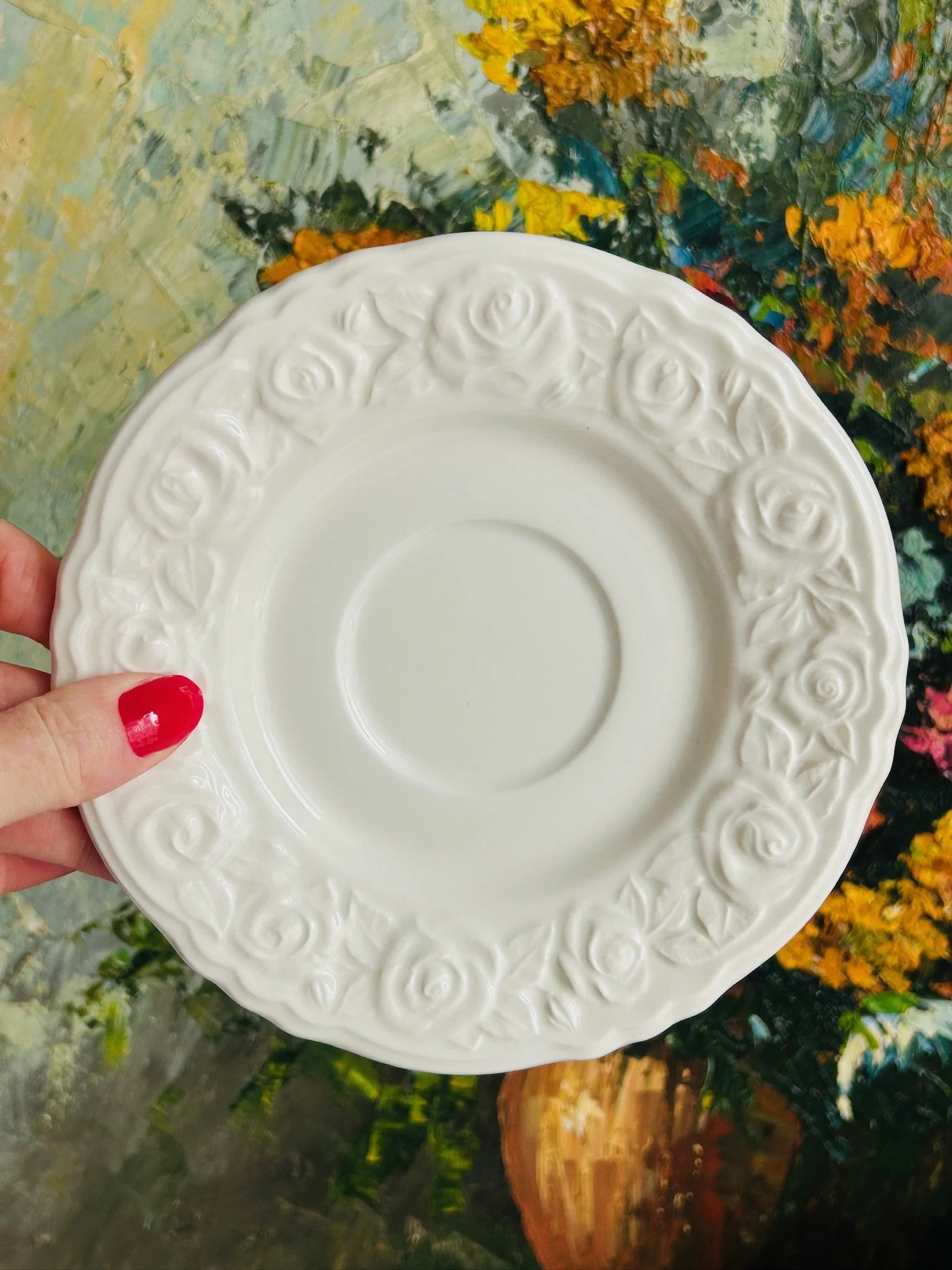 Underside of the saucer held in hand, showing the circular foot ring and raised rose motif around the edge.