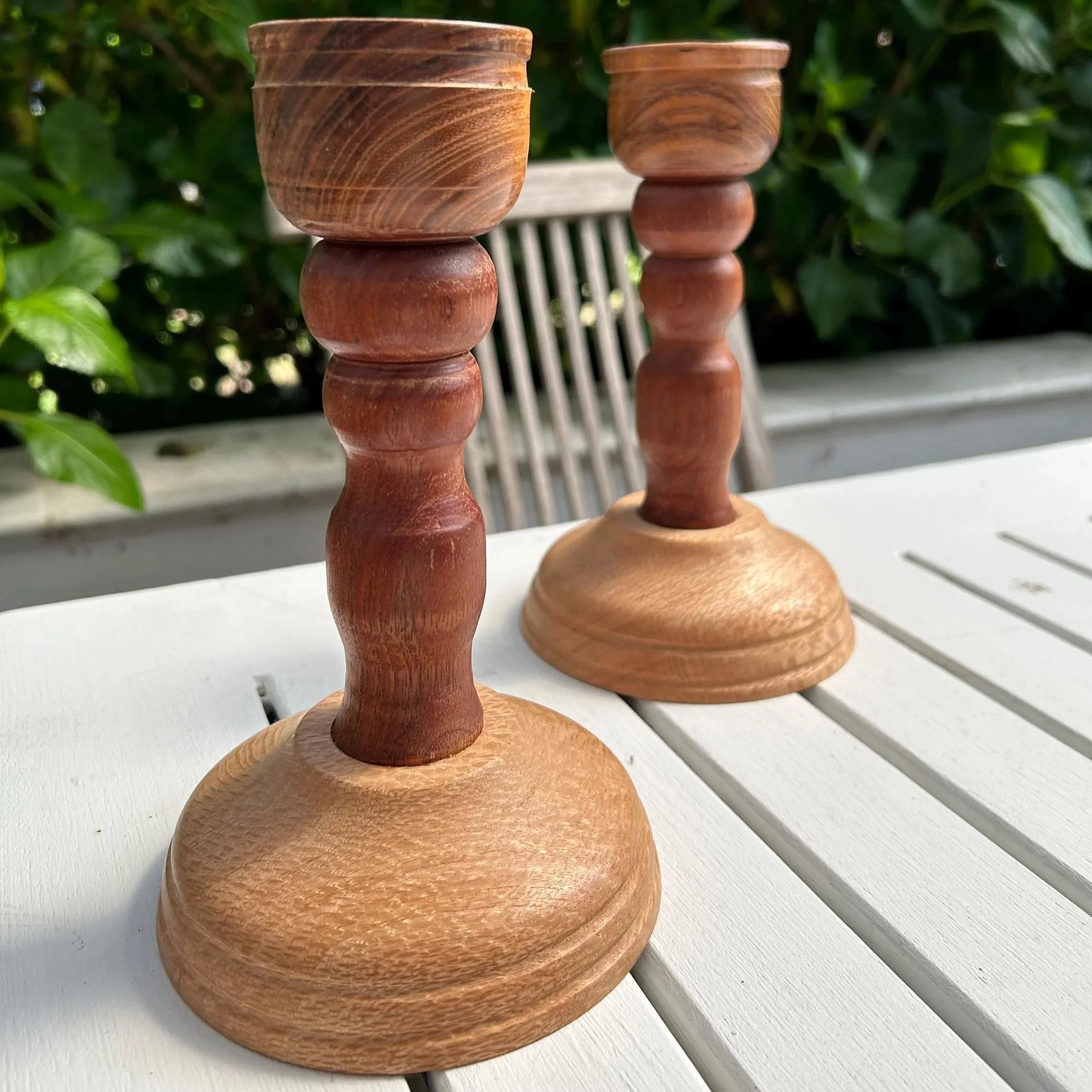 Pair of wooden candleholders standing on outdoor table, showing full height and tones