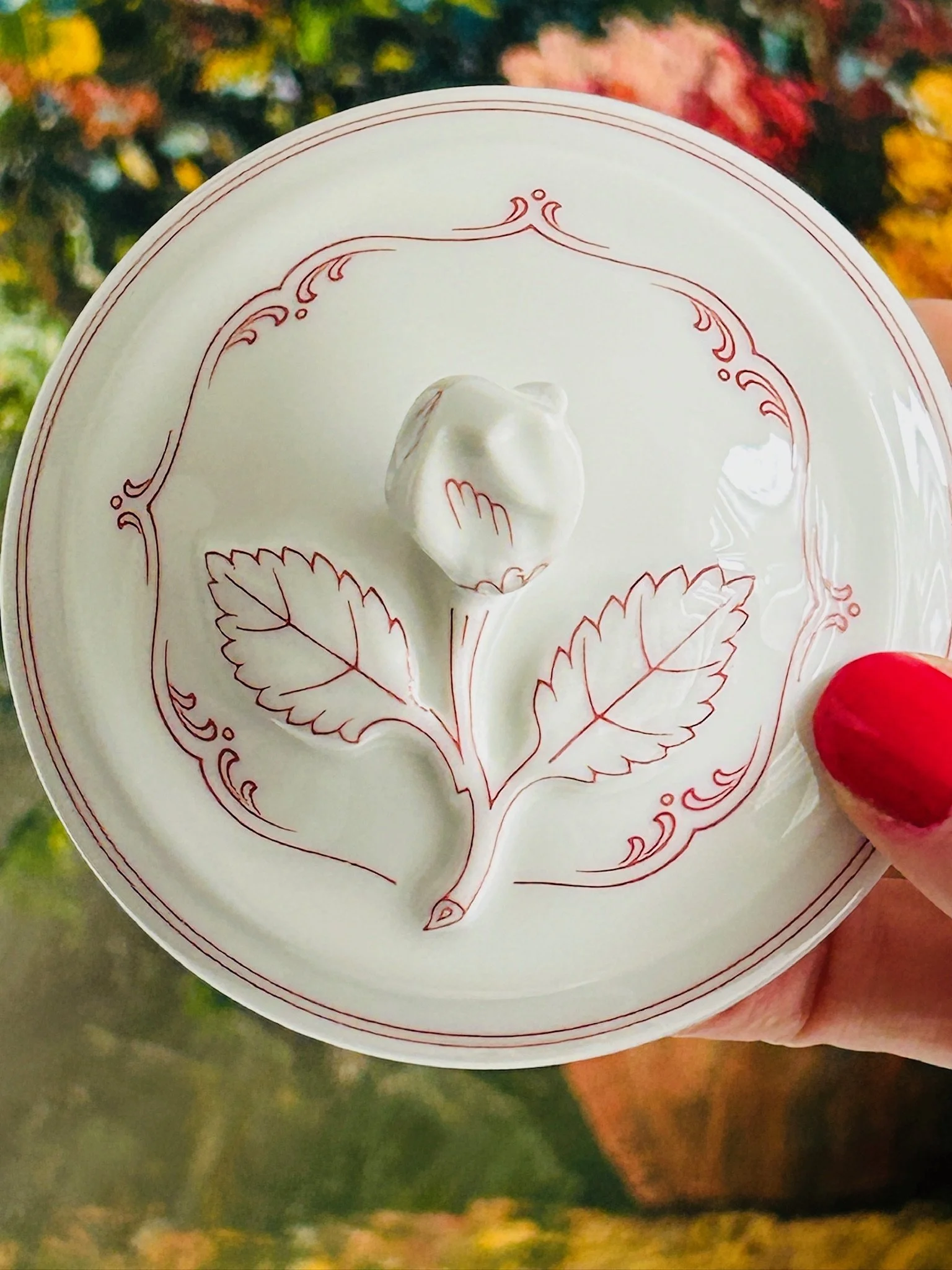Top view of the lid showing the leaf finial and pinkish-red floral design arranged around the centre.