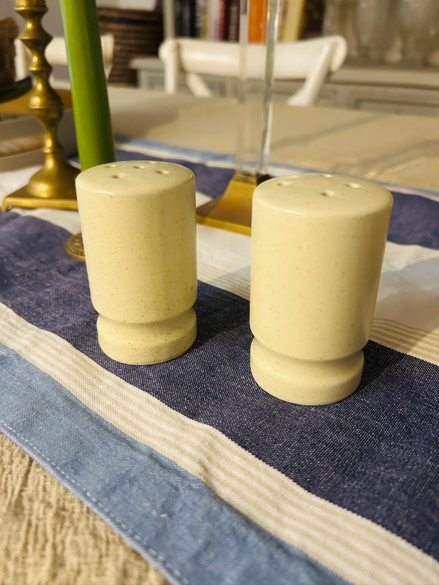 Pair of cream speckled ceramic salt and pepper shakers standing on a blue cloth, showing their simple cylindrical form and softly stepped bases