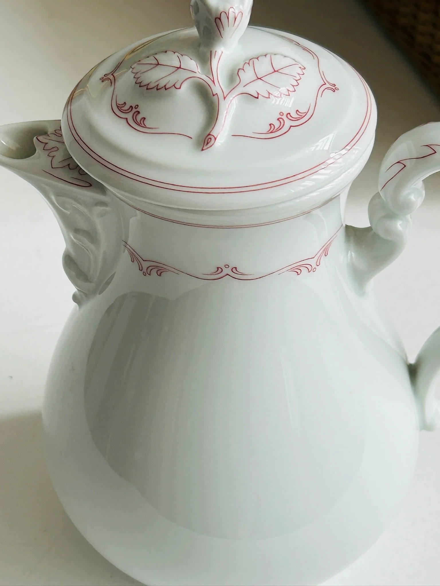 Close-up of the upper body and lid edge, showing the pinkish-red border pattern and sculpted spout.