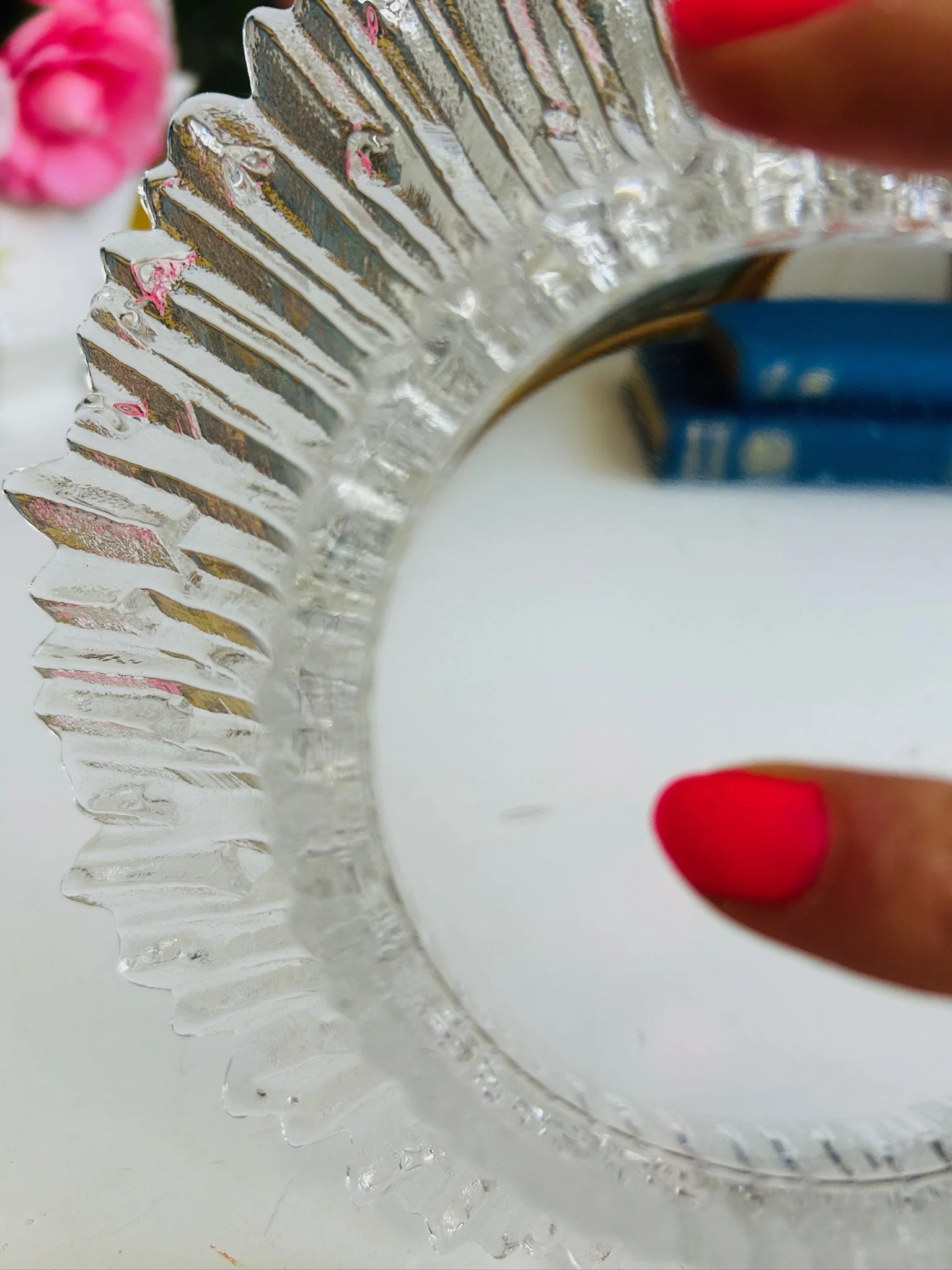 Clear Finnish ice glass dish held face-on against a floral oil painting backdrop