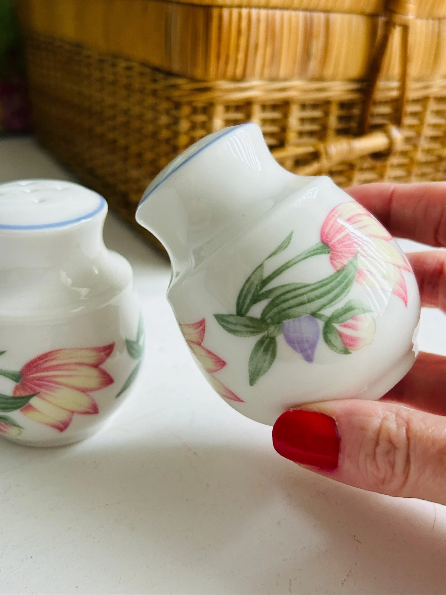 One floral shaker held in hand at an angle, showing the curved shape and pink, yellow, and purple flower motif