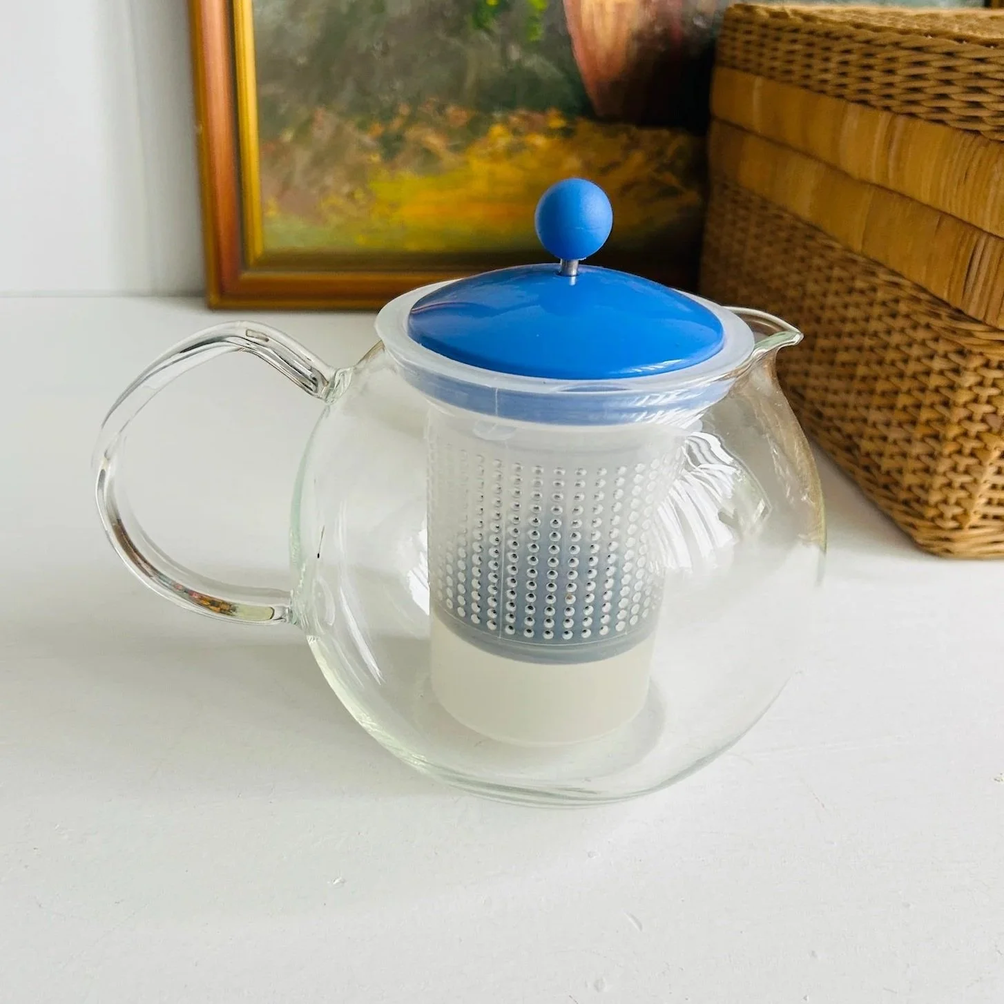 Front view of vintage Bodum Assam tea press with clear borosilicate glass body, blue lid, blue knob, and white mesh infuser inside.
