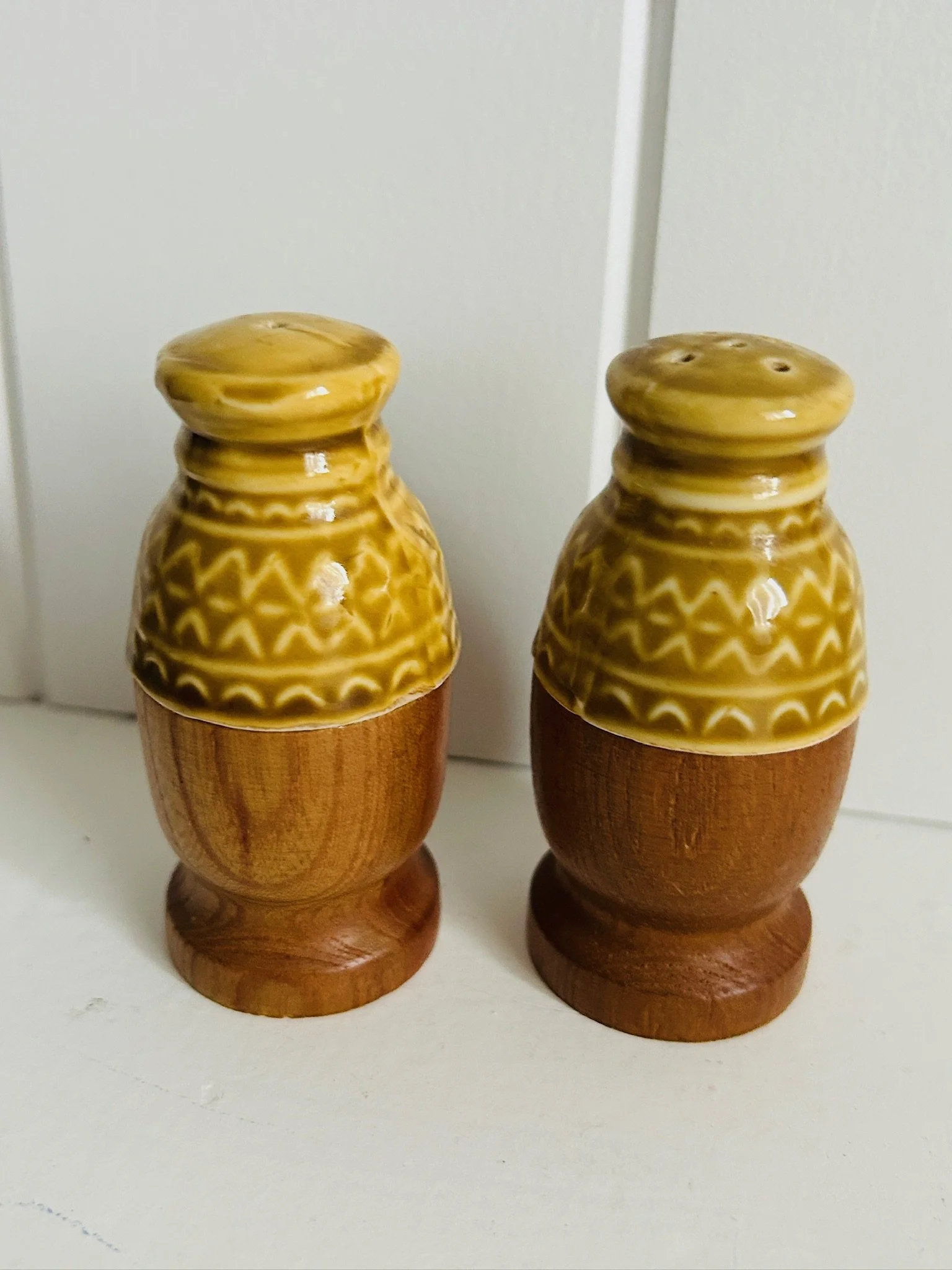 Pair of vintage salt and pepper shakers with mustard yellow ceramic tops and turned wooden bases shown side by side