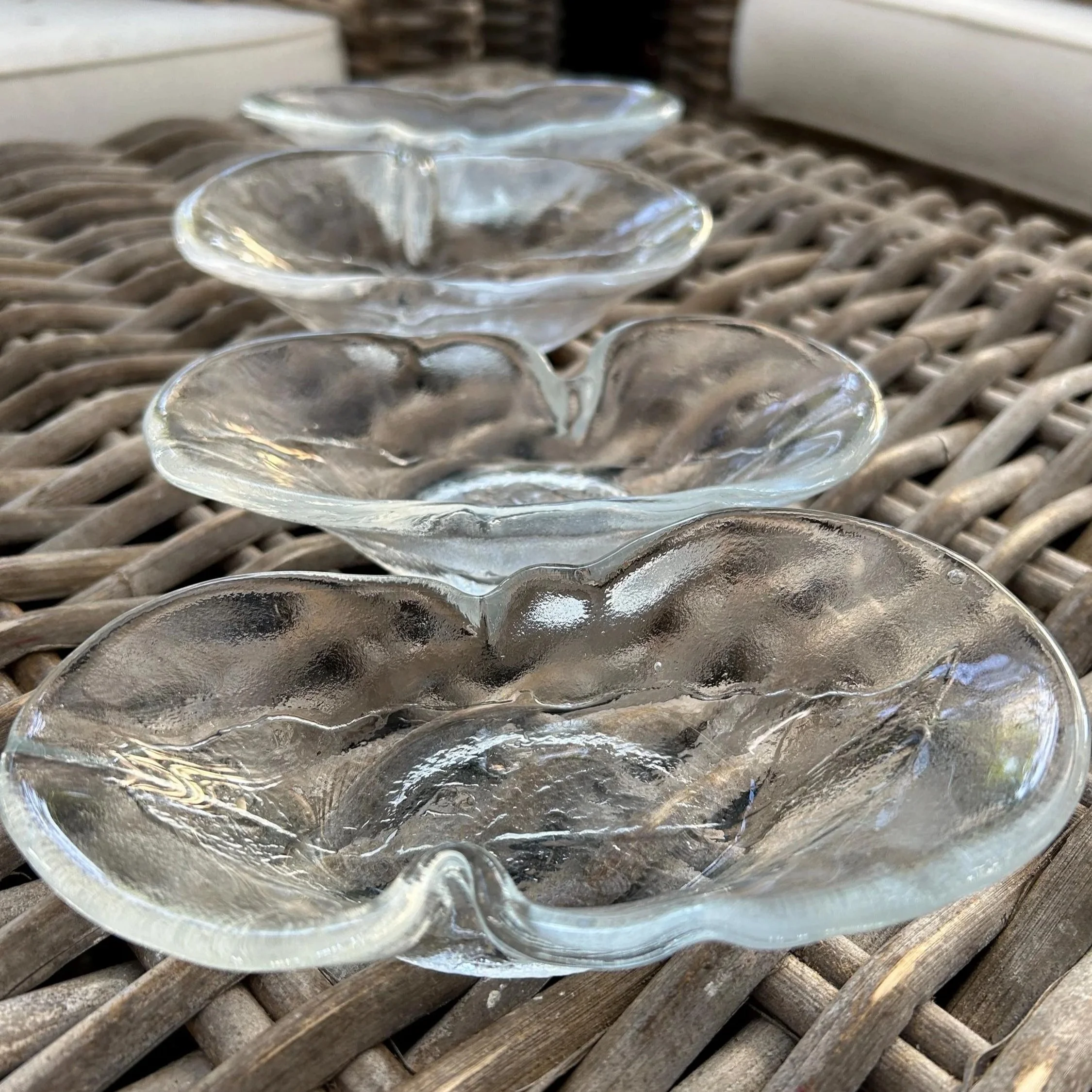 Side view of all four Kosta Boda avocado dishes stacked in a row on wicker chair