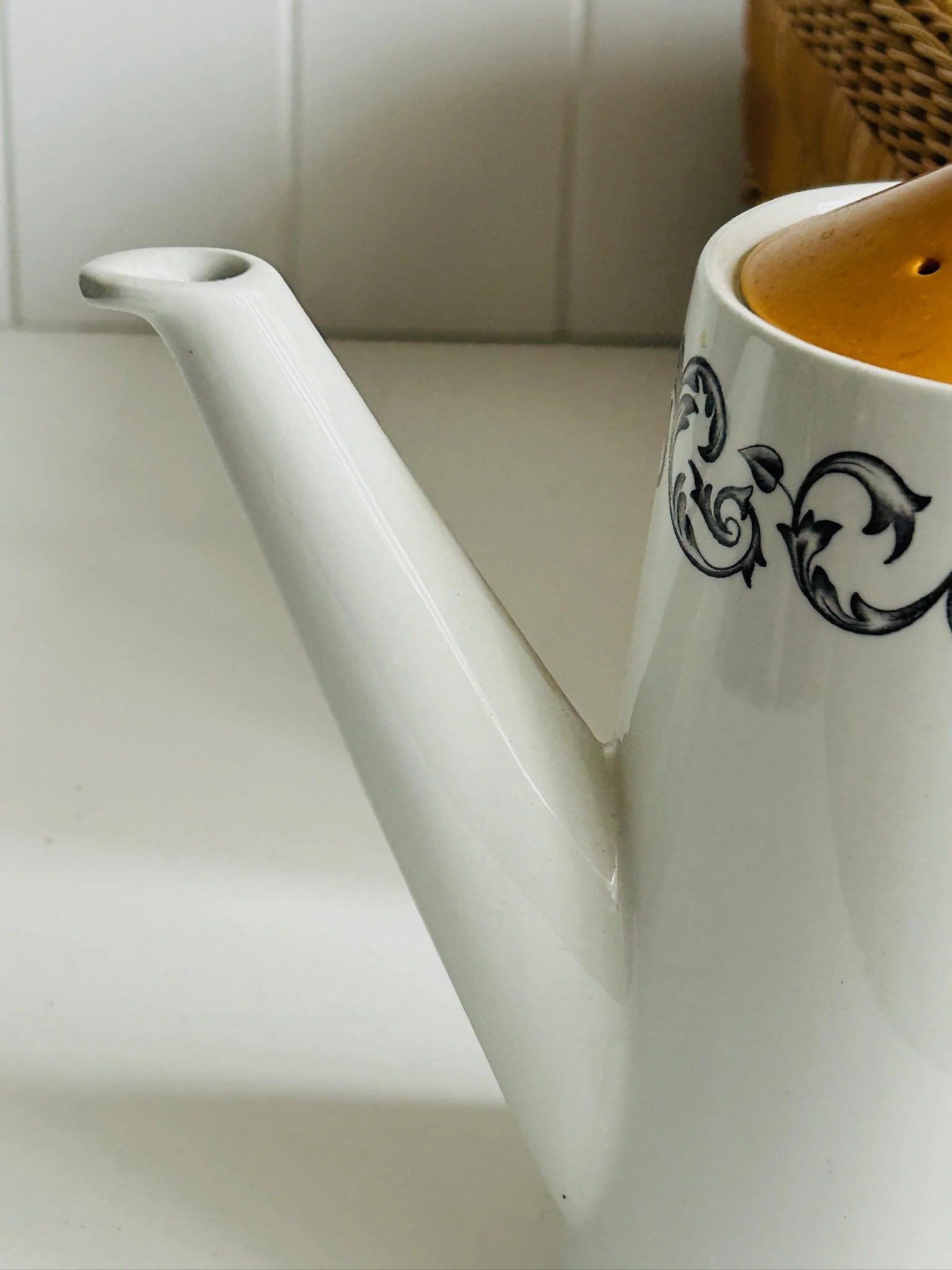 Detail of the coffee pot’s long white spout and upper rim, showing the elegant shape and black baroque scroll pattern.