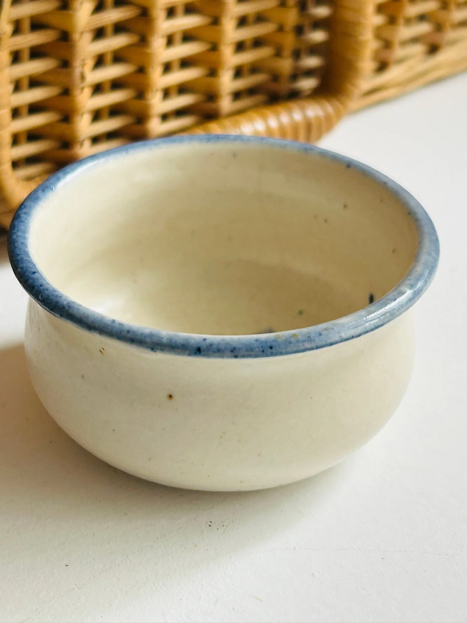 Side view of the small beige ceramic bowl showing the rounded form and denim blue rim