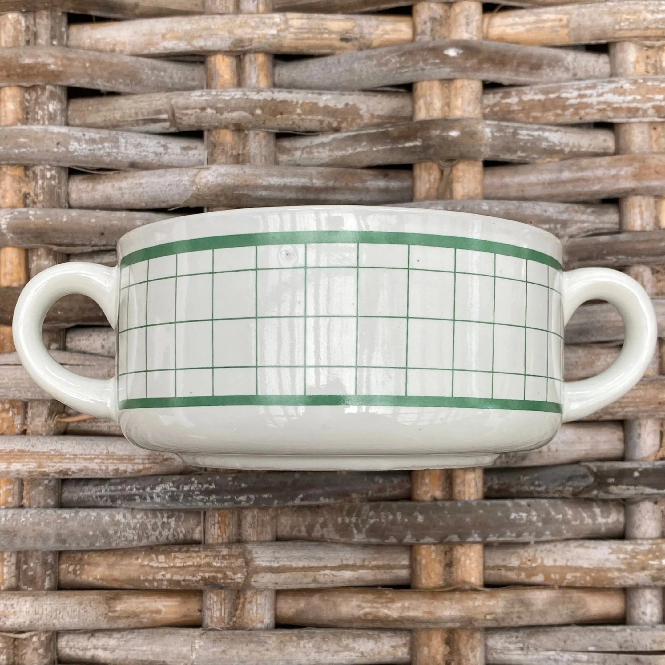 Green grid pattern soup mug with twin handles on woven surface