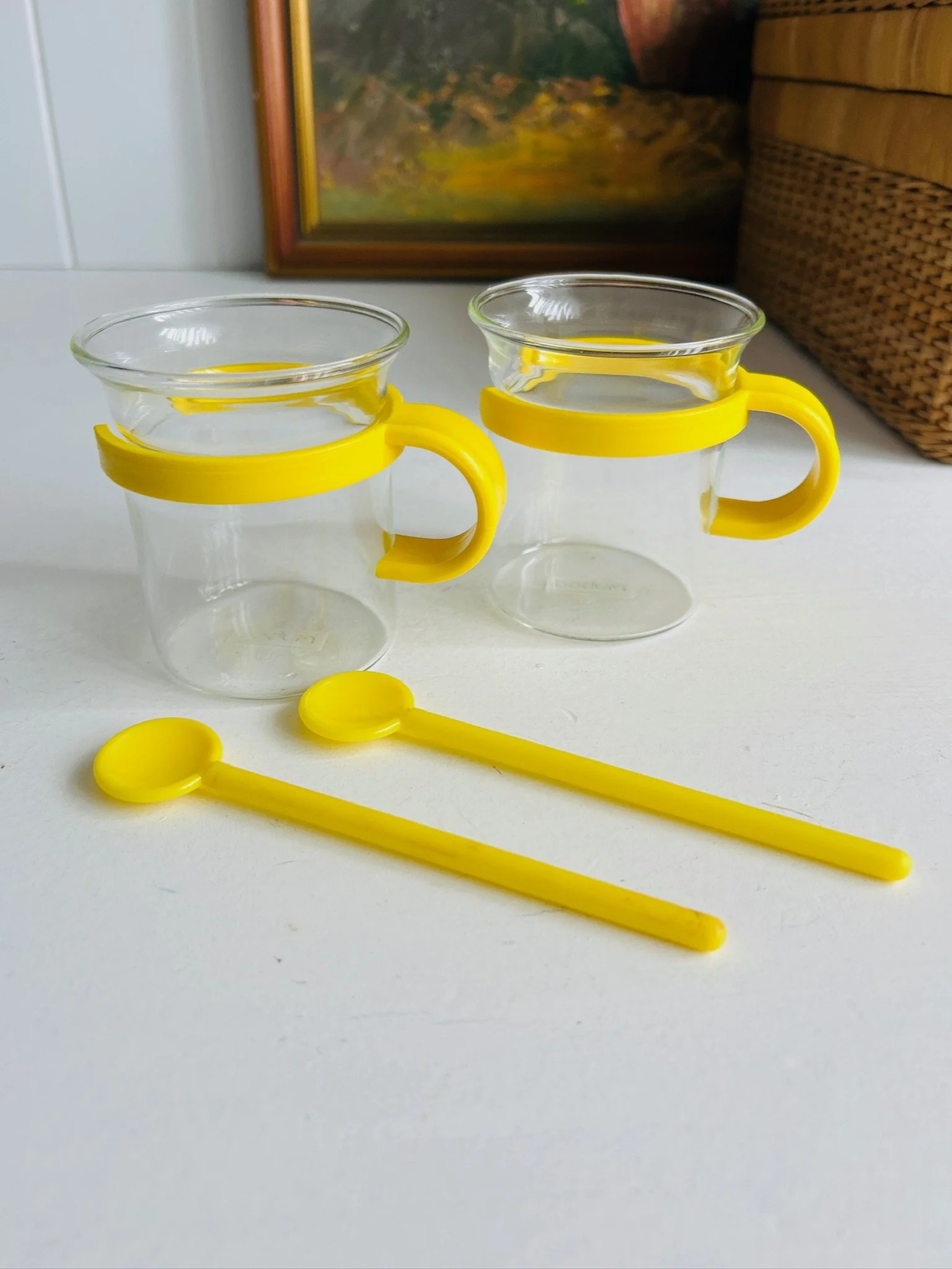 Two Bodum Picard cups with yellow holders and matching yellow spoons displayed together on a white surface.