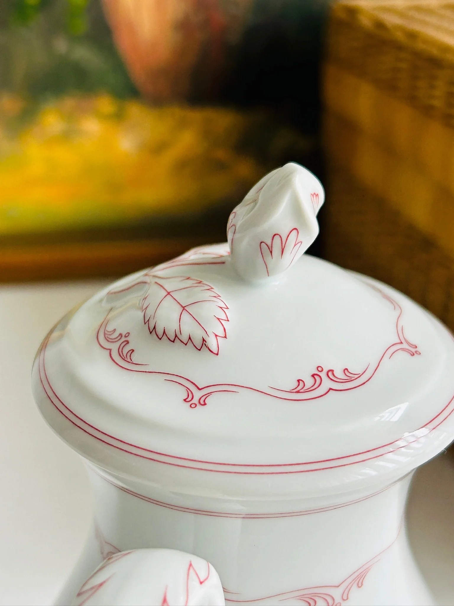 Close-up of the lid and finial from the side, showing the raised leaf knob and fine red scroll border.