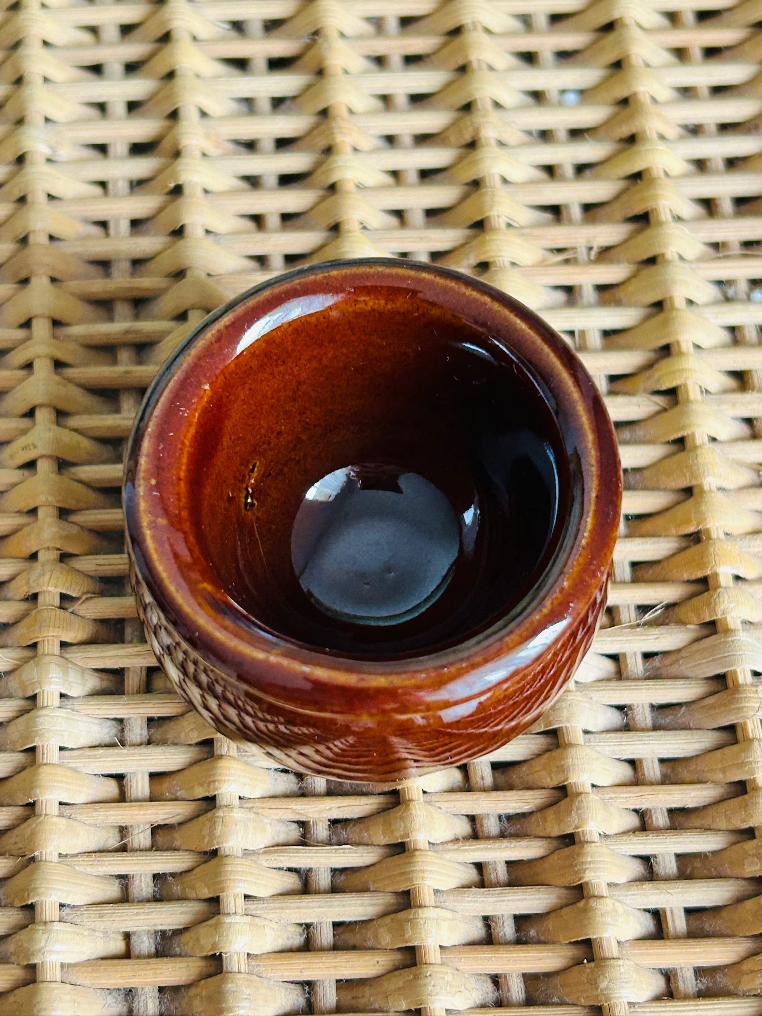 Overhead view of the salt cellar placed on wicker, showing the circular opening and deep brown glazed interior