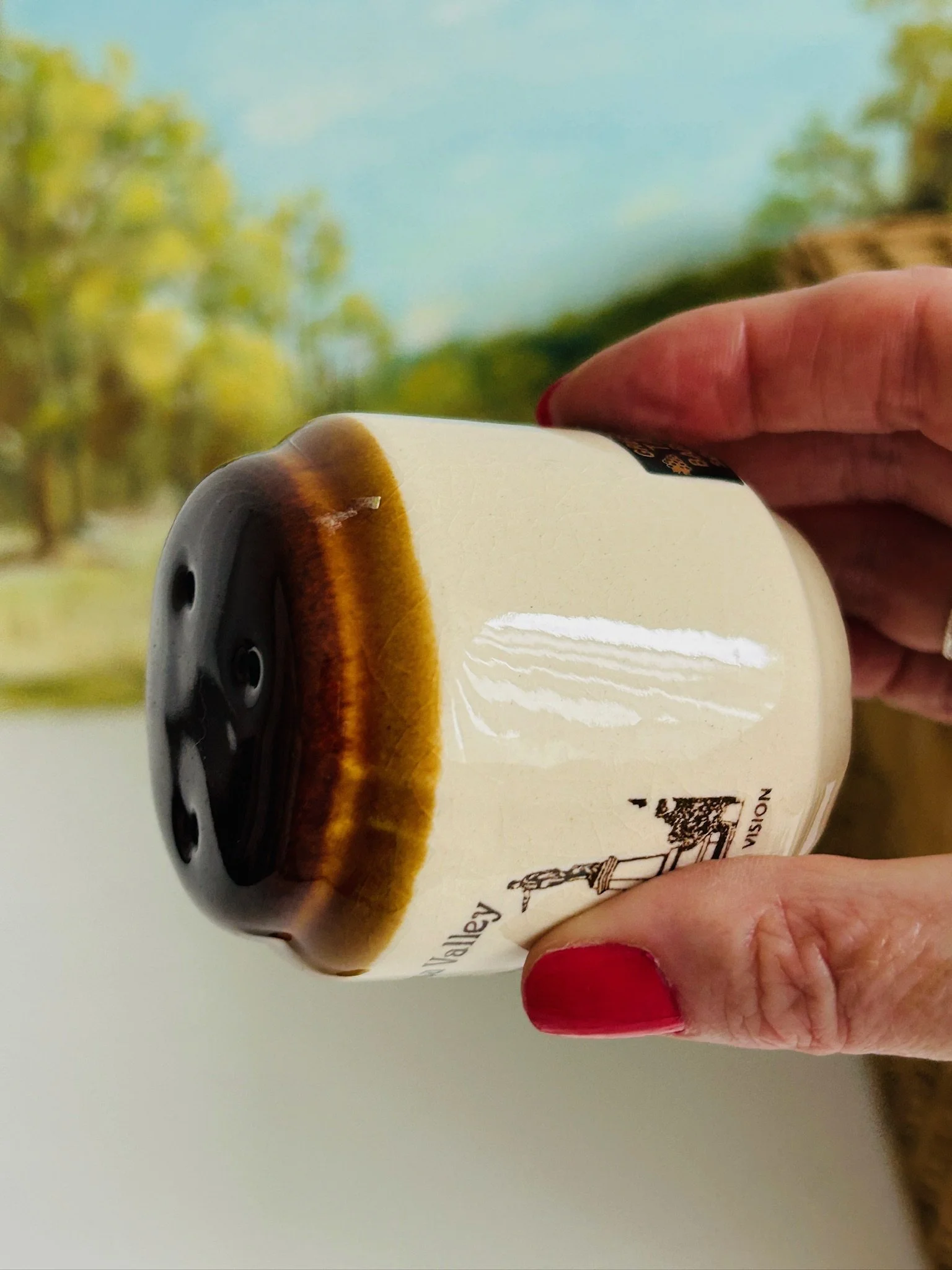 Shaker tilted in hand to show the glossy brown glazed top, side profile, and smooth cream ceramic body.