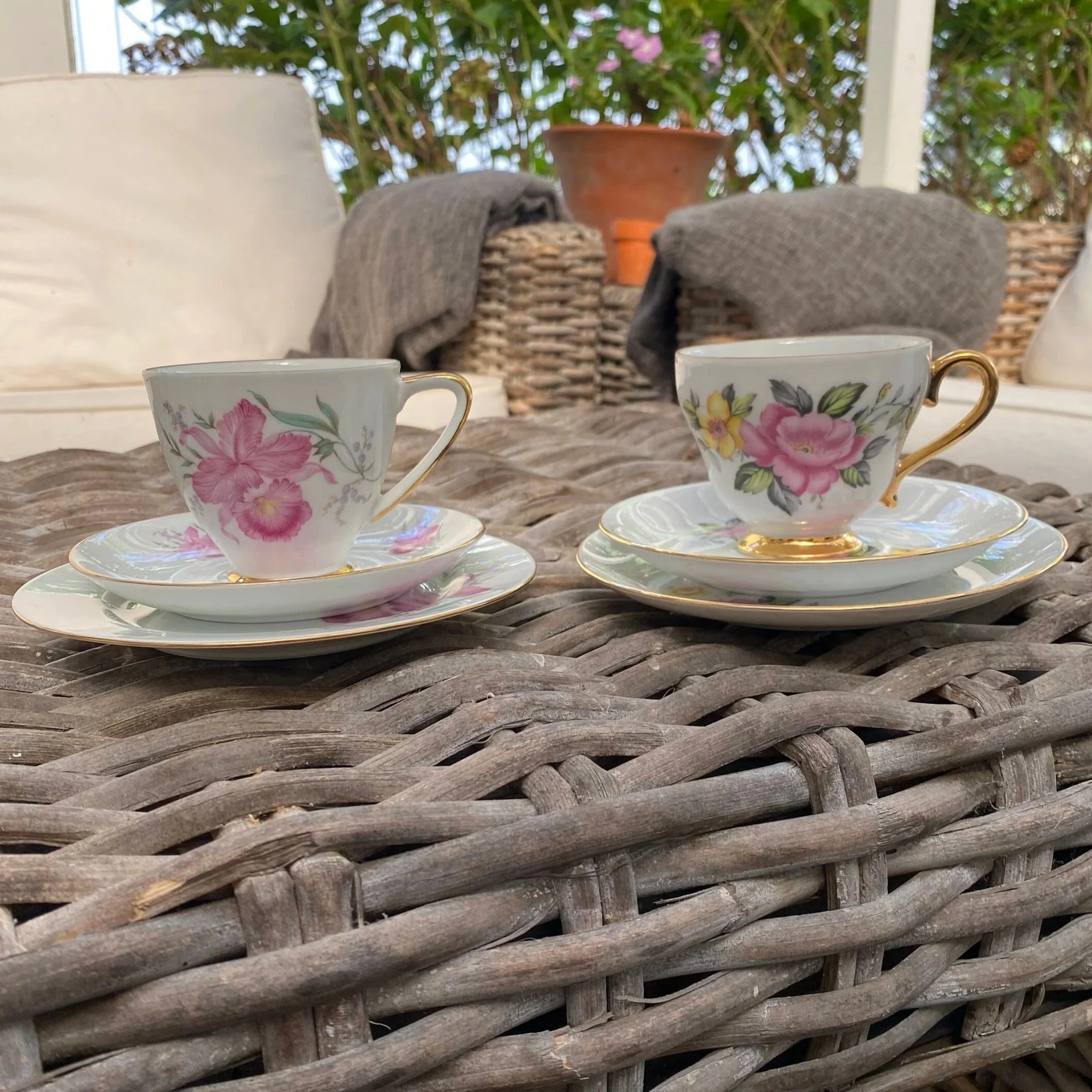 Both tea trios displayed side by side on a woven table, showing the coordinating floral designs