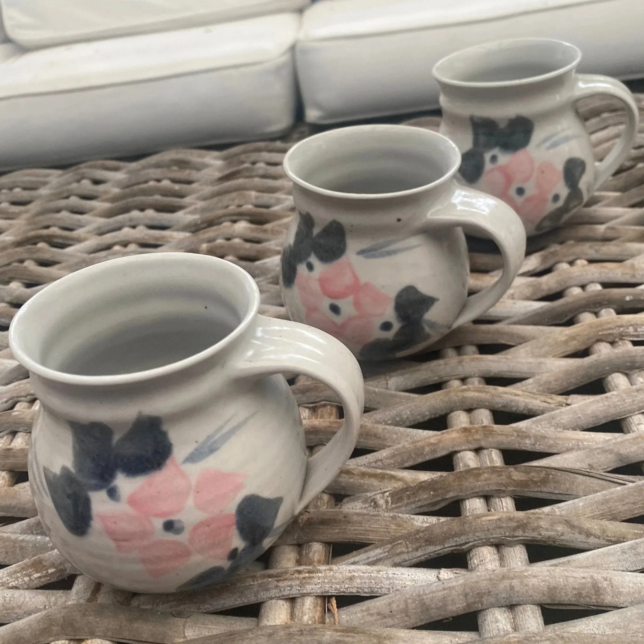 Angled front view of all three mugs, lined up on woven table