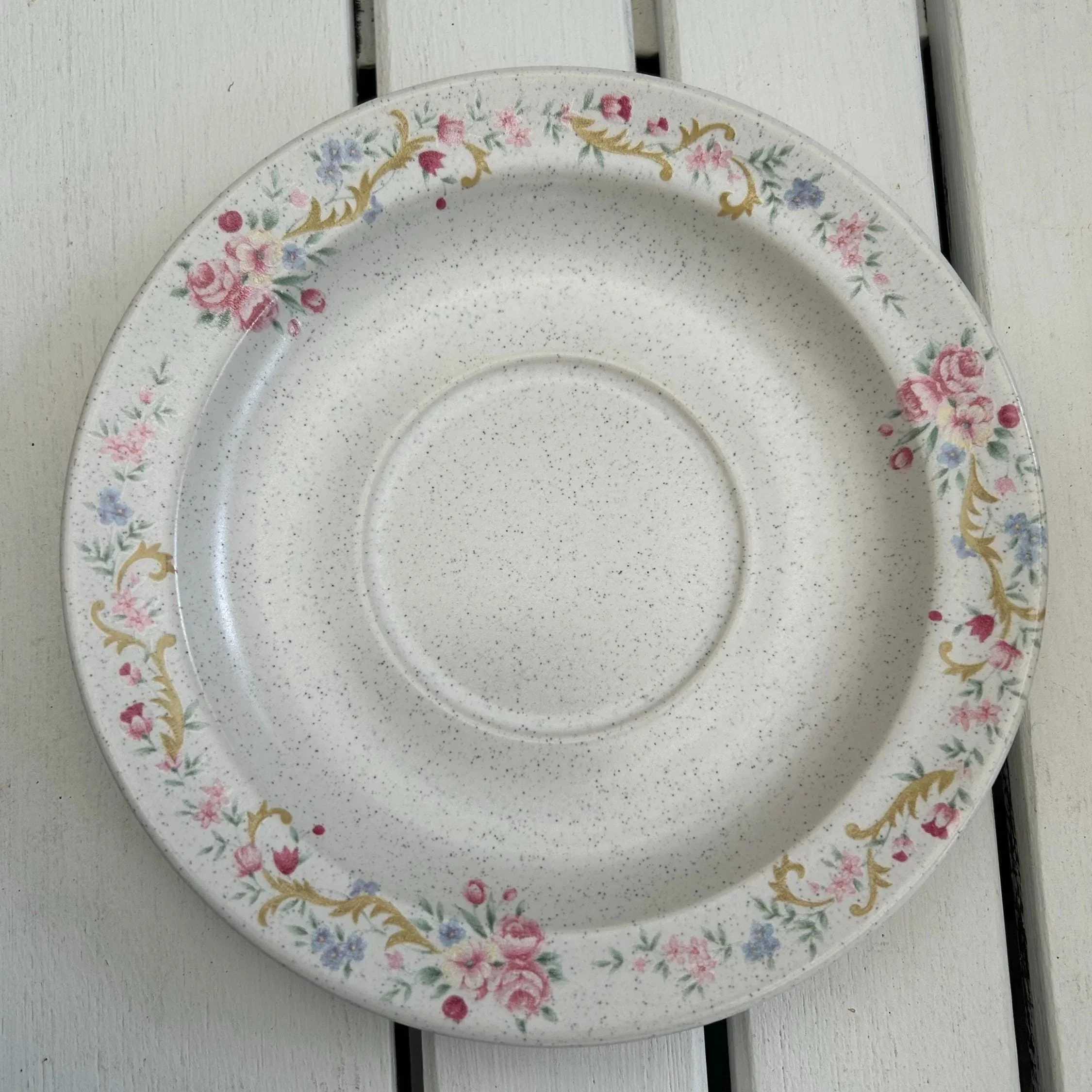 Single saucer showing full floral rim design on speckled beige stoneware