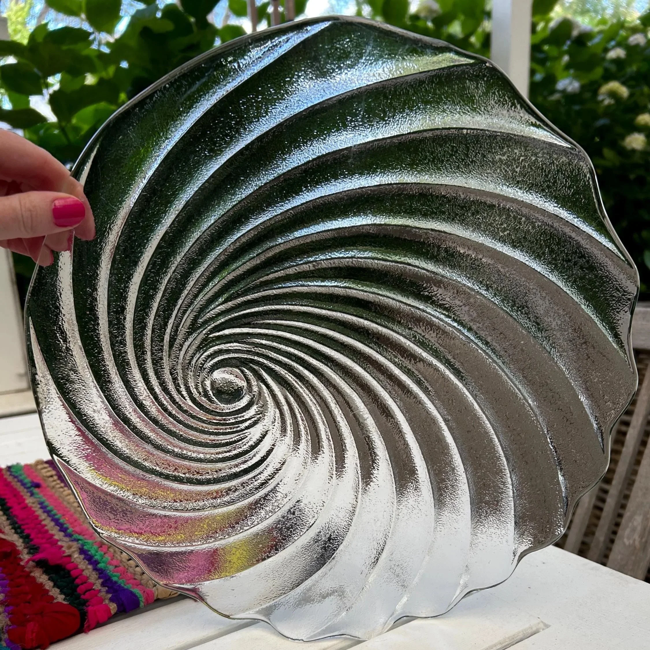 Round mouth-blown Italian glass platter with spiral shell design held in hand.