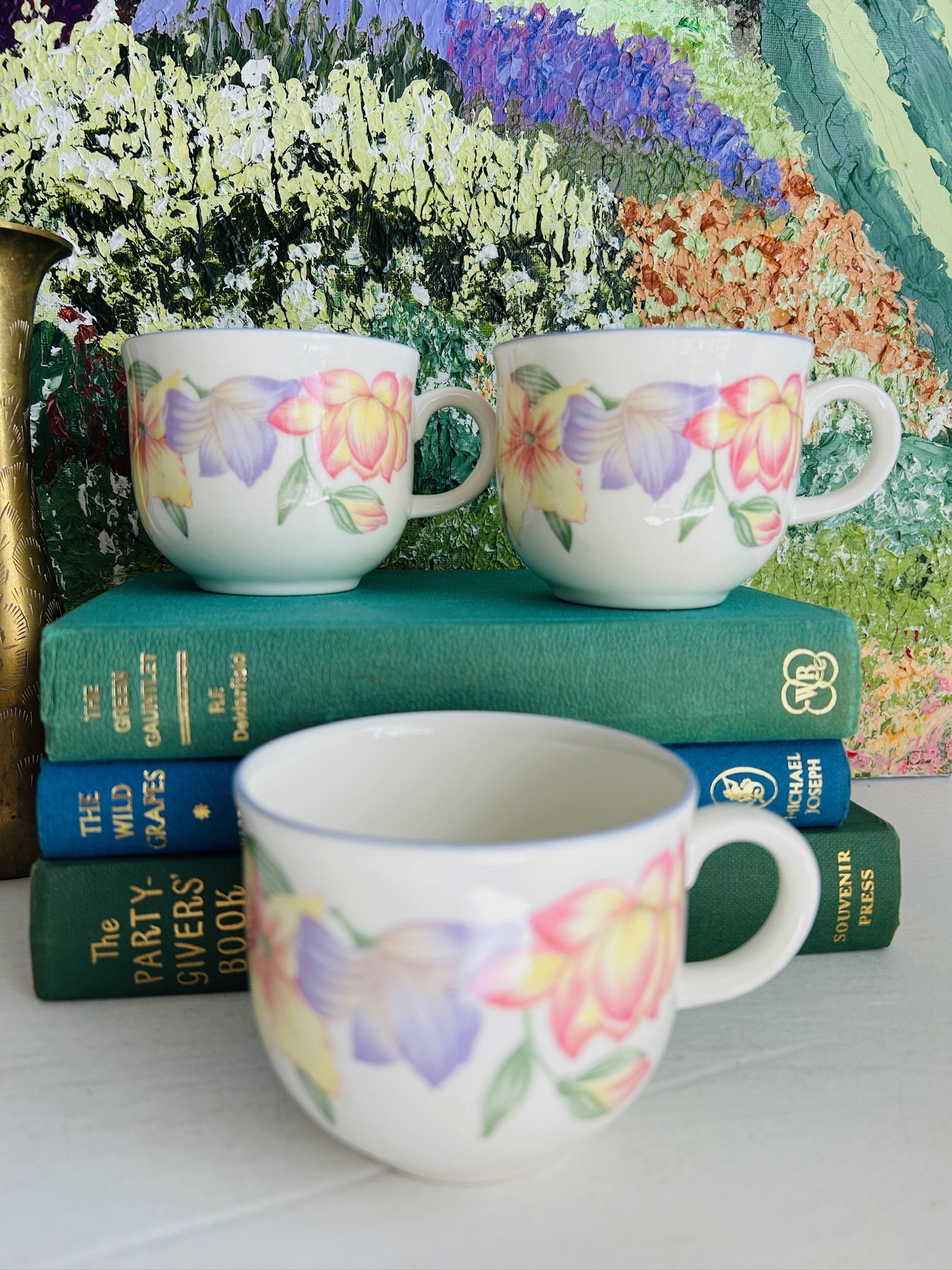 Three vintage Royal Doulton Expressions Blooms teacups displayed together on stacked books, showing the soft floral pattern in pink, yellow, and lilac