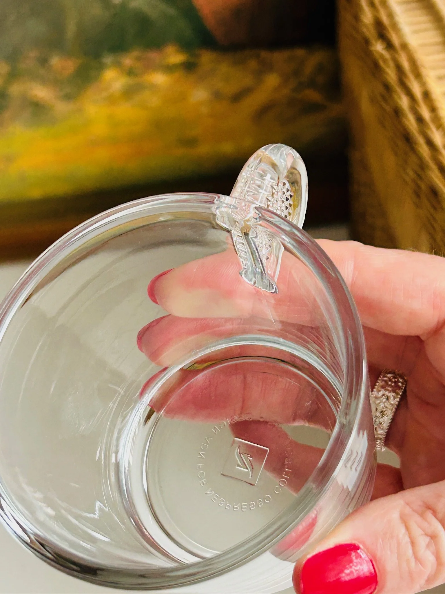 Top-down angled view of a single Nespresso glass cup being held, showing the rim, handle and base mark
