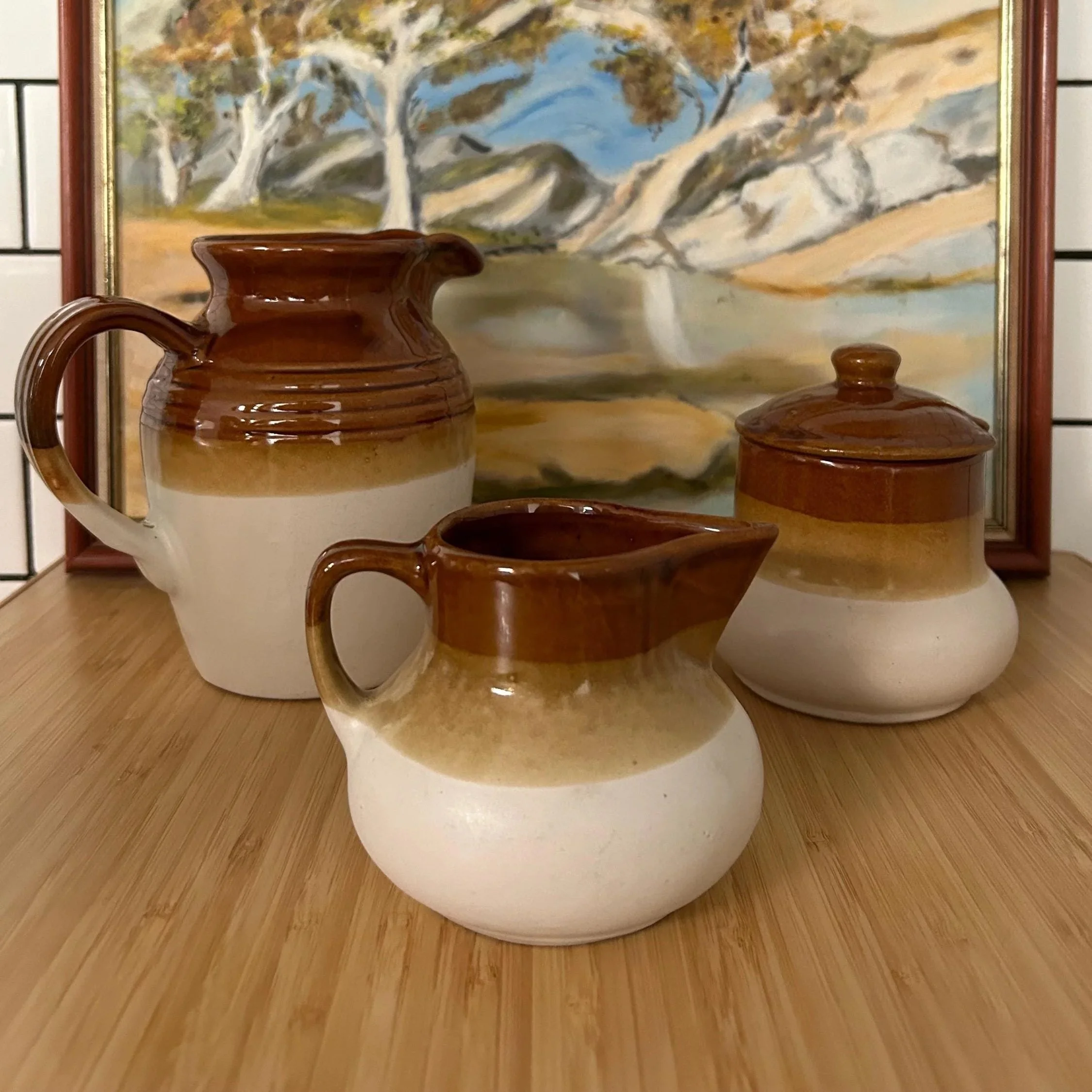 Full set of tri-toned pitcher, creamer, and sugar bowl styled on timber bench with landscape art in background