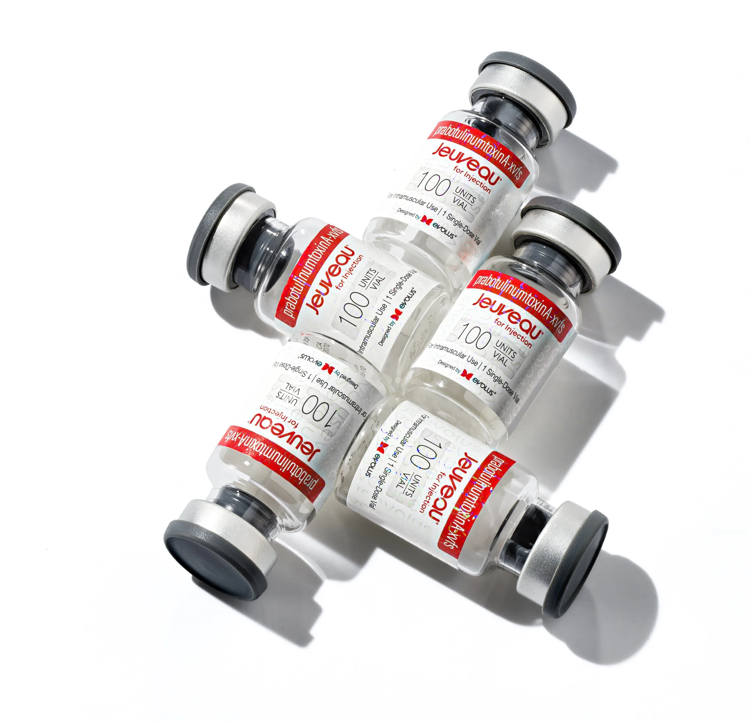 Four vials of Jevau, a botulinum toxin injection, arranged on a white surface with shadows.