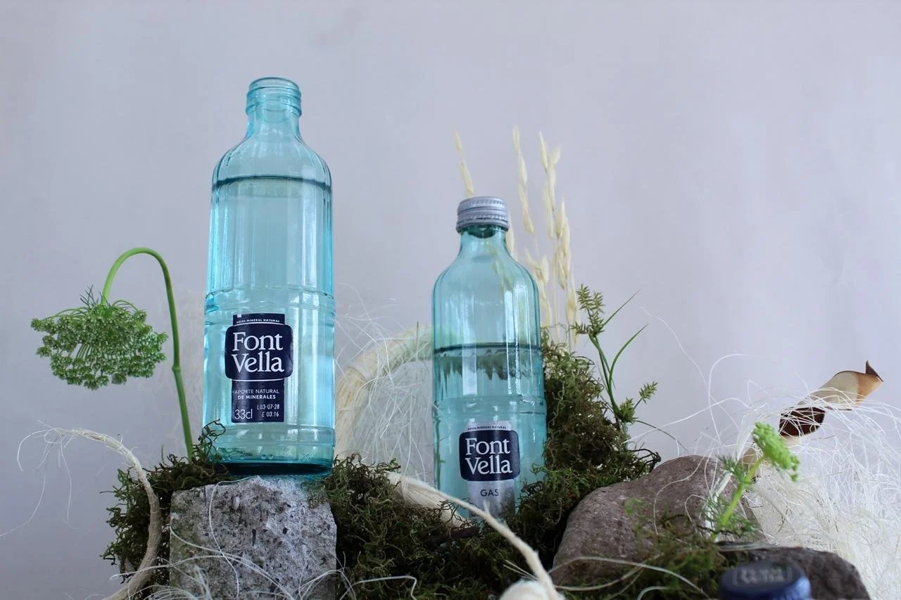 Low-angle view of Font Vella water bottles within a contemporary floral installation using moss, rocks and natural fibers by Ceci Bordas.